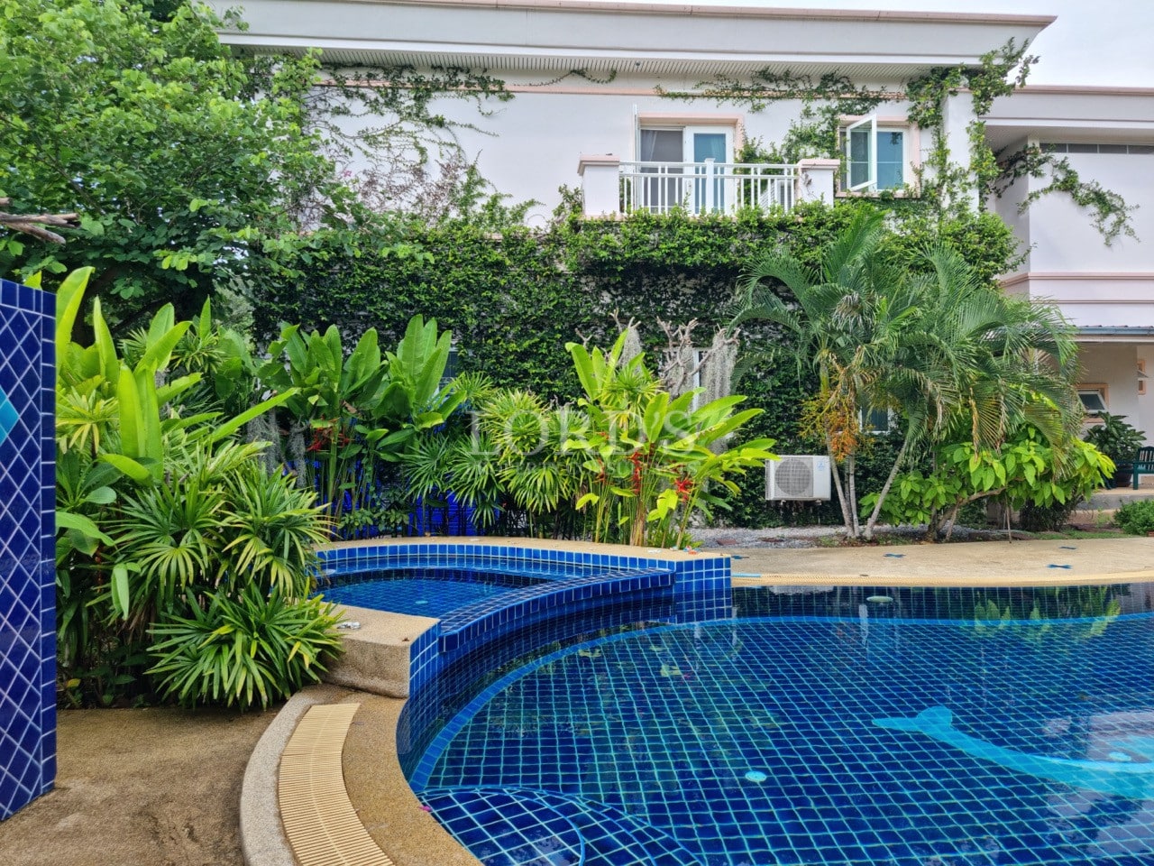 Luxury villa swimming pool with blue mosaic tiles surrounded by lush tropical garden and greenery.
