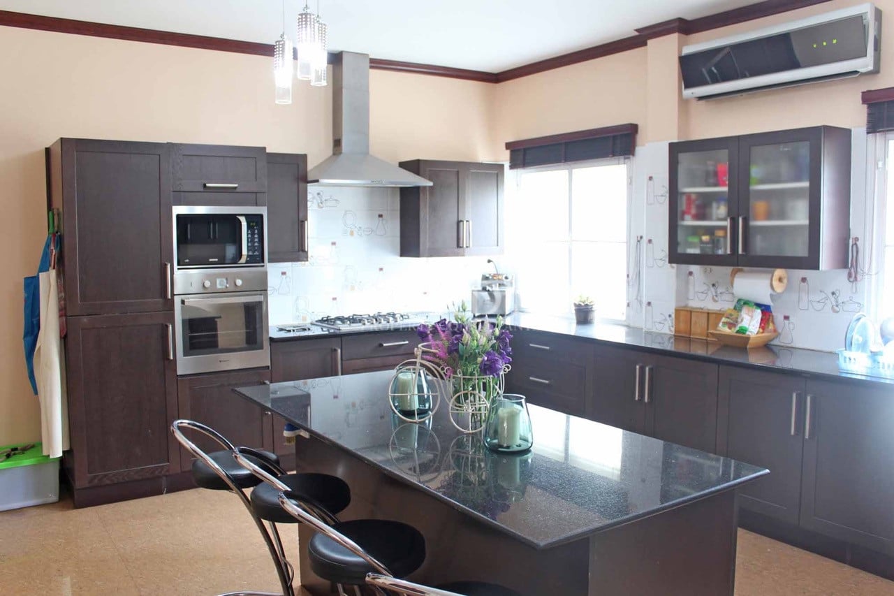 Modern kitchen with dark wood cabinets, black granite island, built-in oven, and stainless steel appliances.