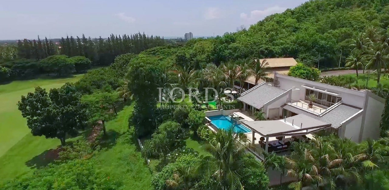 Aerial view of a luxury villa with a private swimming pool surrounded by lush greenery and a golf course.