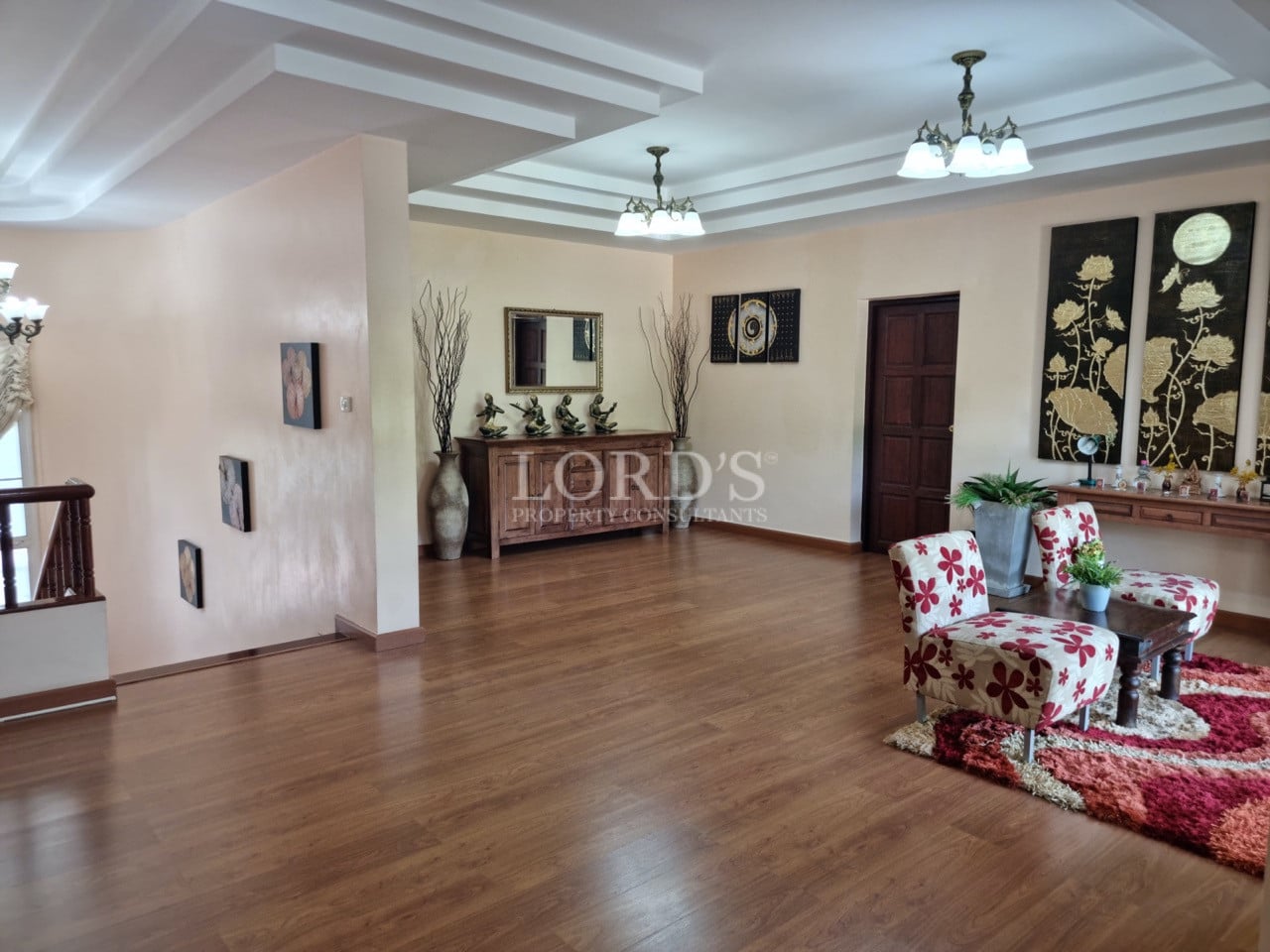Elegant living hall with wooden flooring, decorative ceiling lights, and classic accent chairs.