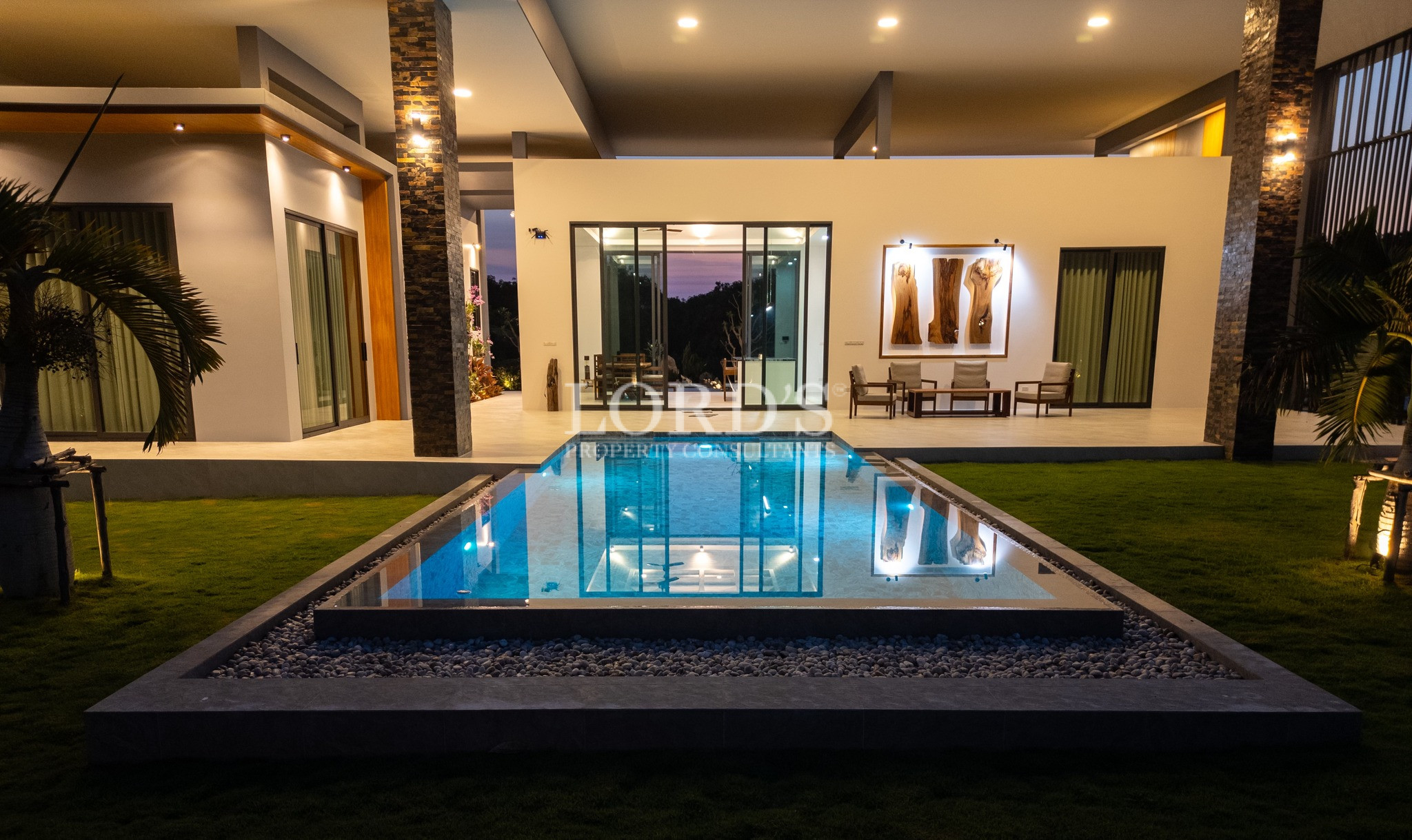 Luxury modern villa with illuminated swimming pool and outdoor seating at night.