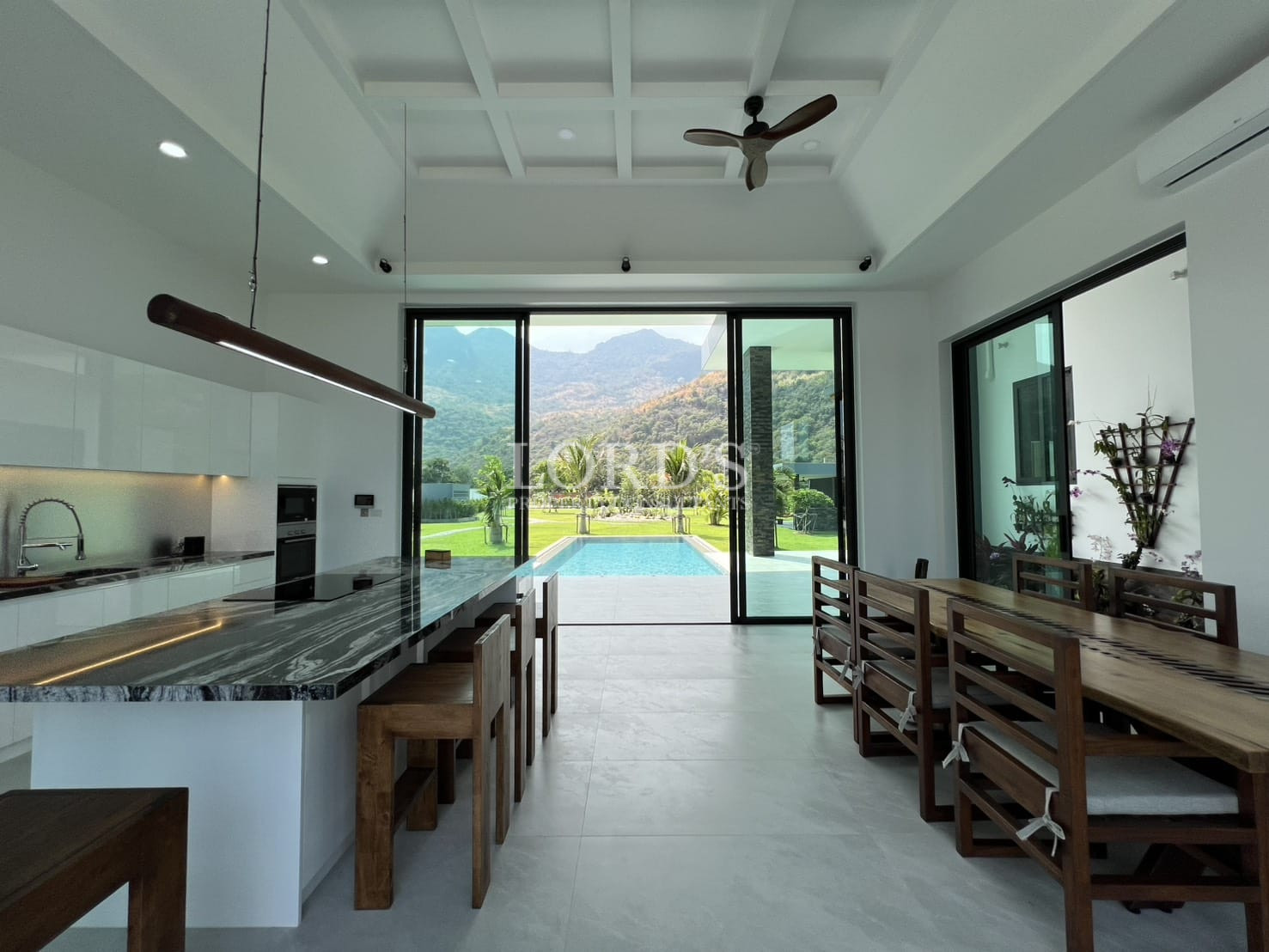 Modern open-plan kitchen and dining area with pool and mountain views through glass doors.