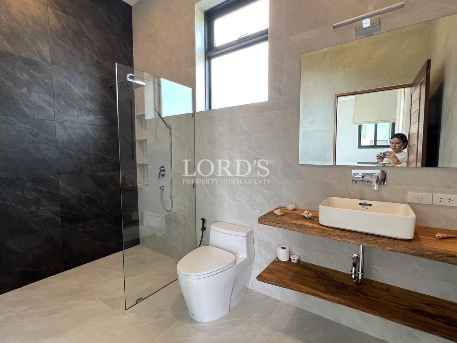 Modern bathroom with glass walk-in shower, floating wooden vanity, and vessel sink.
