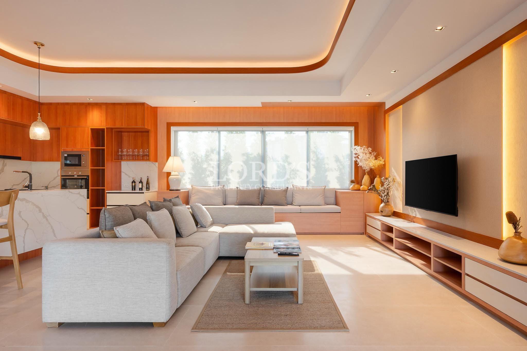 Open-plan living room with sectional sofa, TV wall, and adjoining modern kitchen.