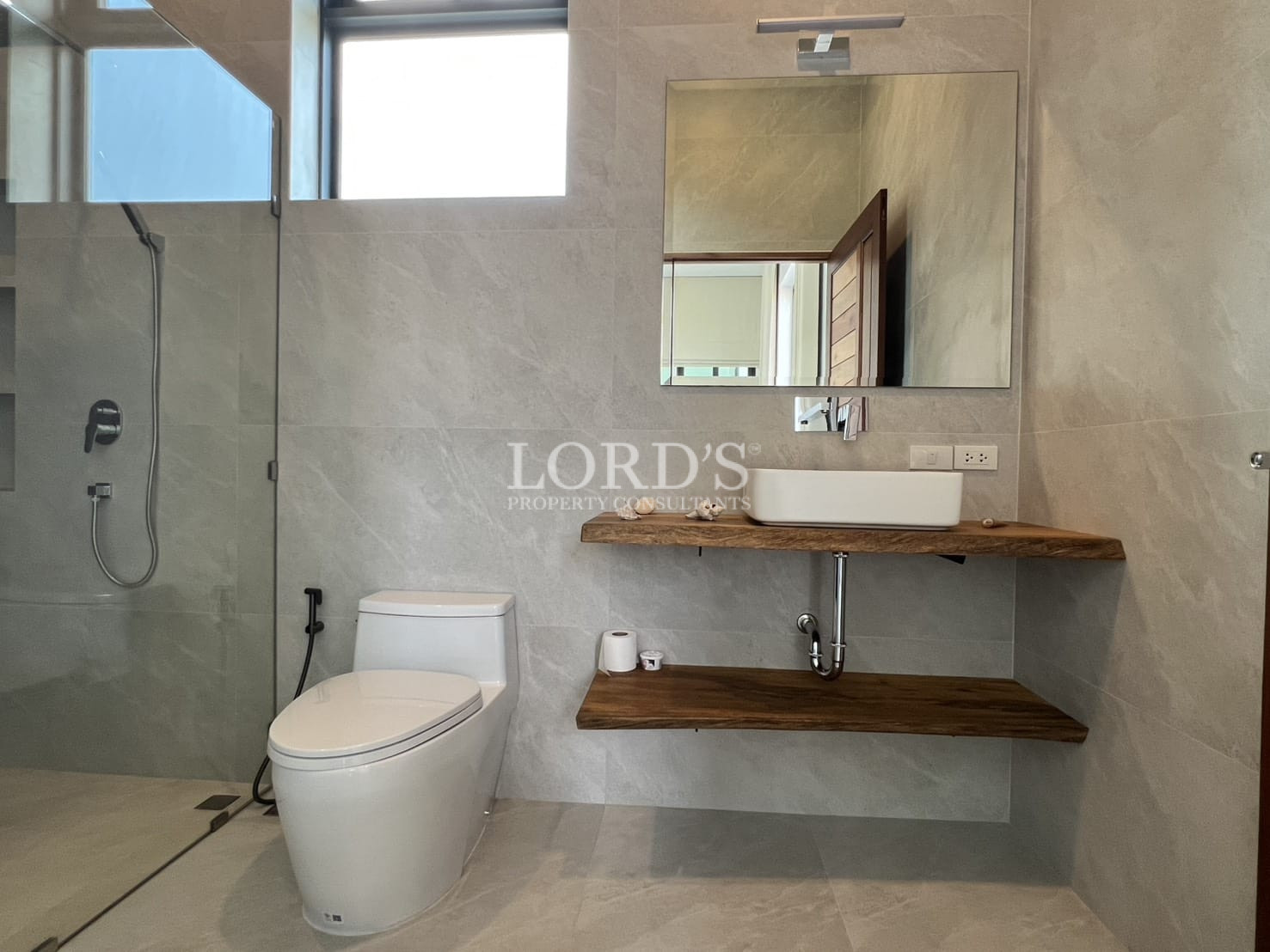 Modern bathroom with wall-mounted wooden vanity, vessel sink, and glass shower enclosure.