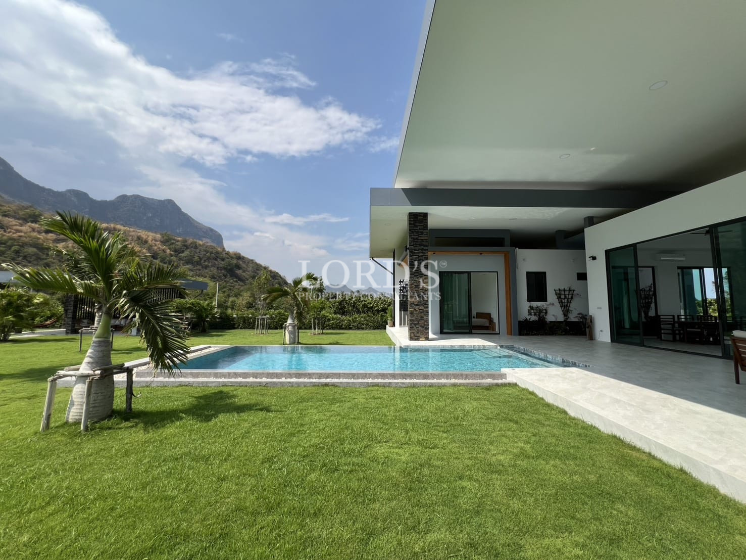 Modern villa terrace with private swimming pool, lawn, and mountain views.