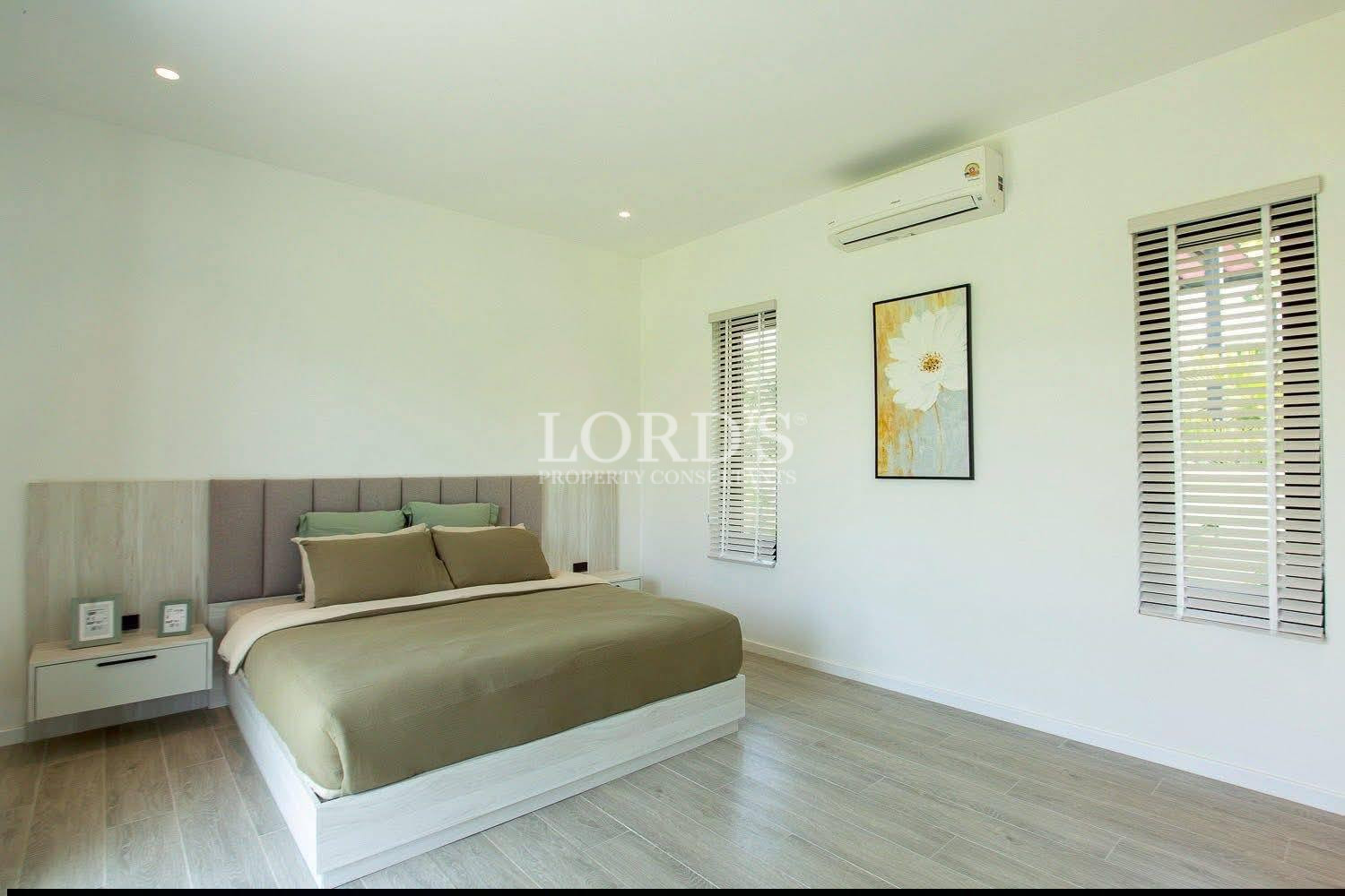 Modern bright bedroom with green bedding, white walls, wooden floor, and window blinds