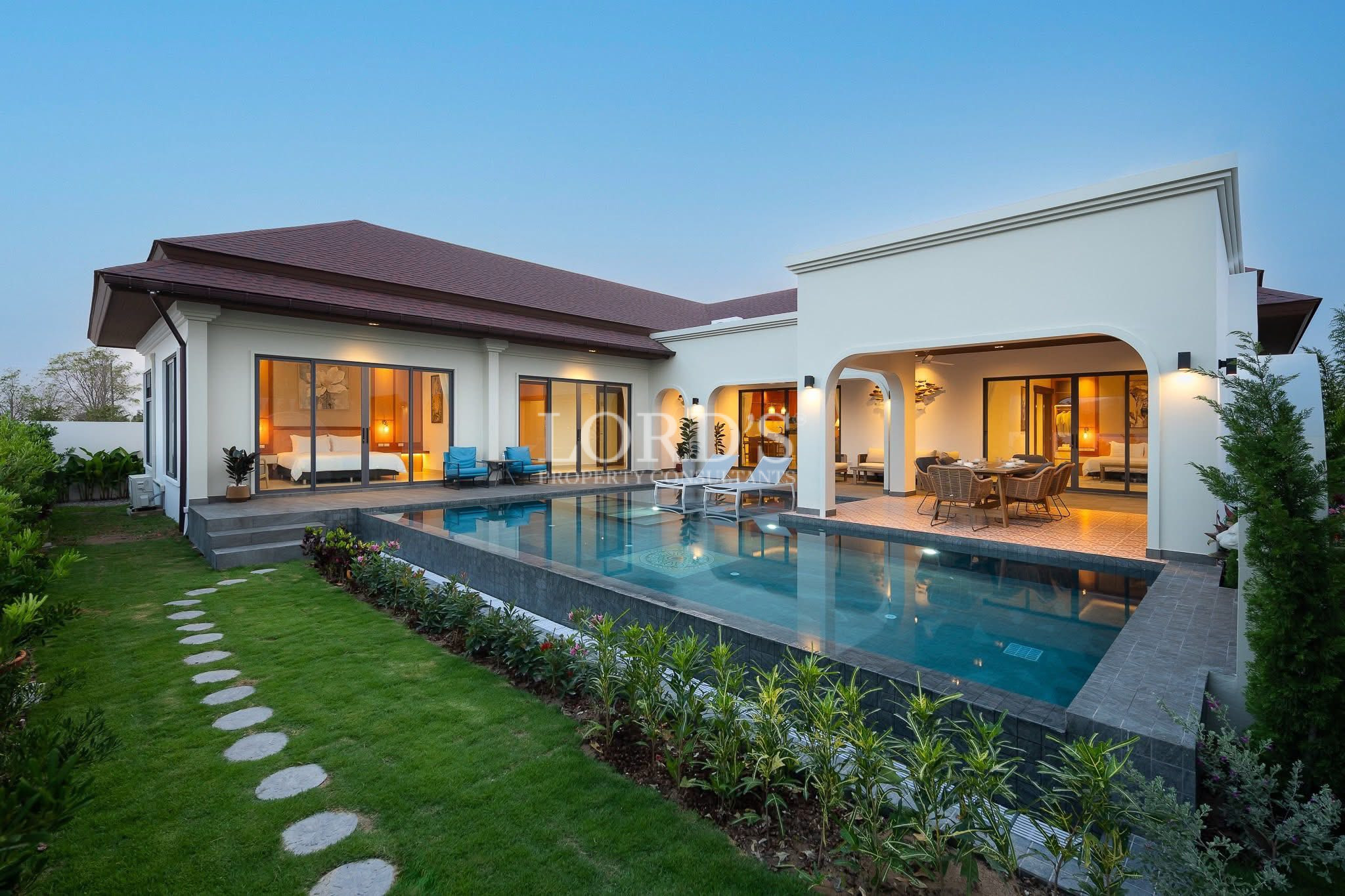 Modern luxury villa with private swimming pool, landscaped garden, and outdoor dining terrace at dusk.