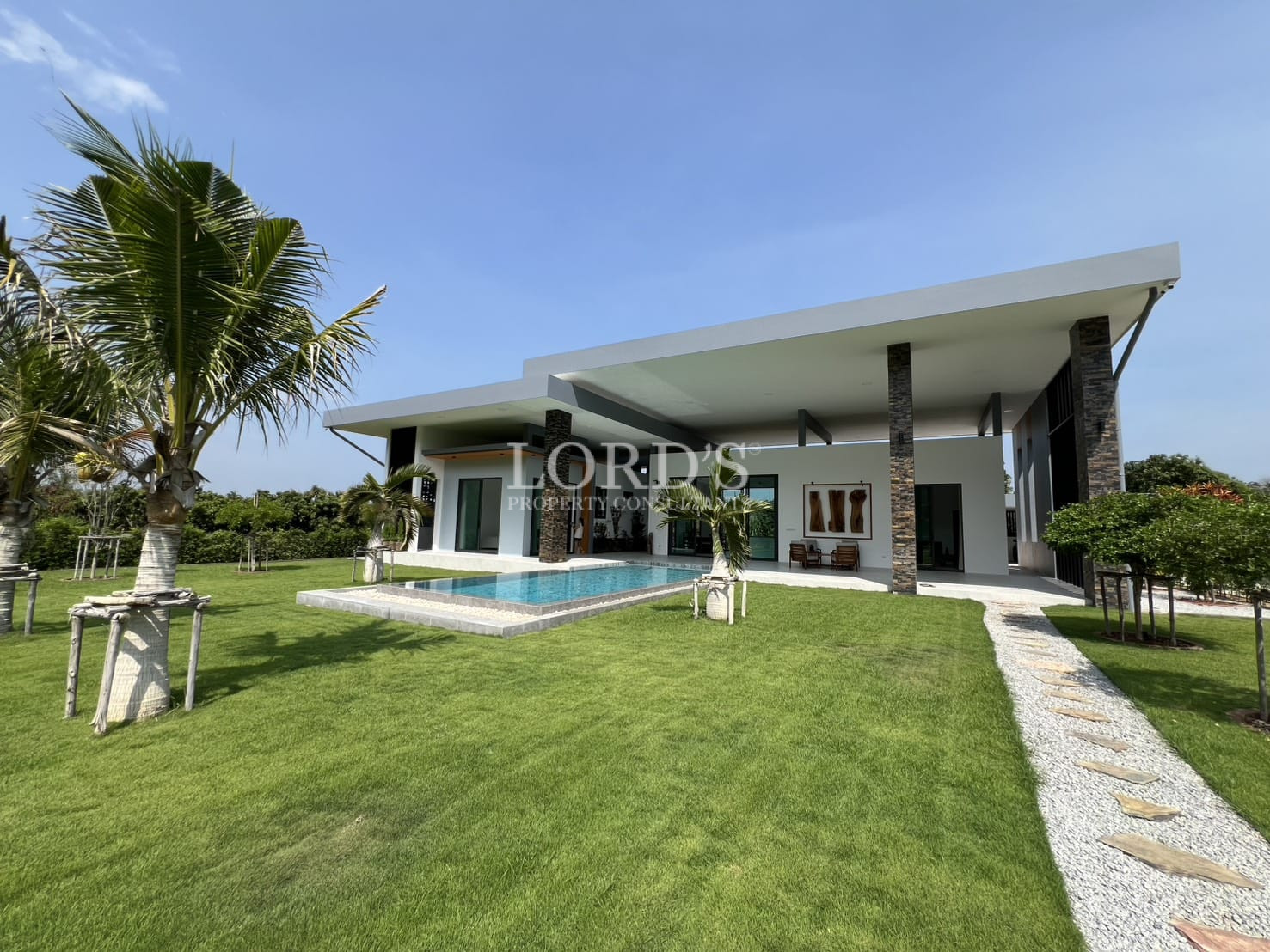Modern single-story villa with private pool, landscaped lawn, and stone pathway.