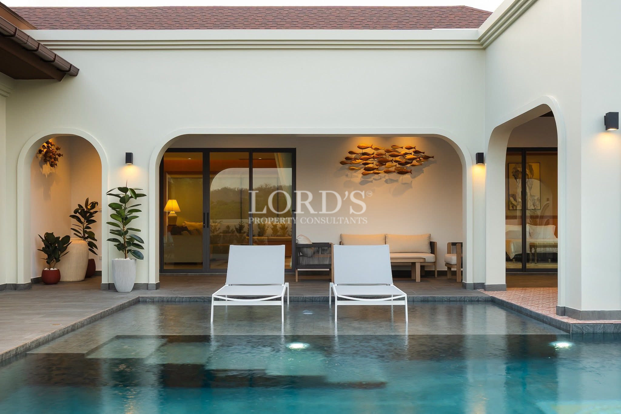 Private villa pool with sun loungers facing a covered outdoor lounge and patio seating area.