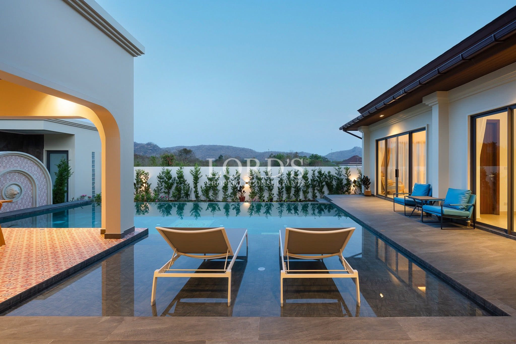 Luxury villa swimming pool at dusk with lounge chairs and outdoor seating area.