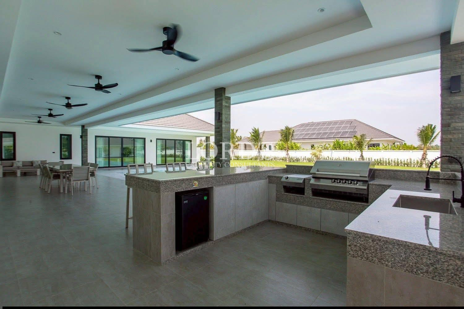 Covered outdoor kitchen and patio area with built-in grill, sink, and dining space overlooking garden.