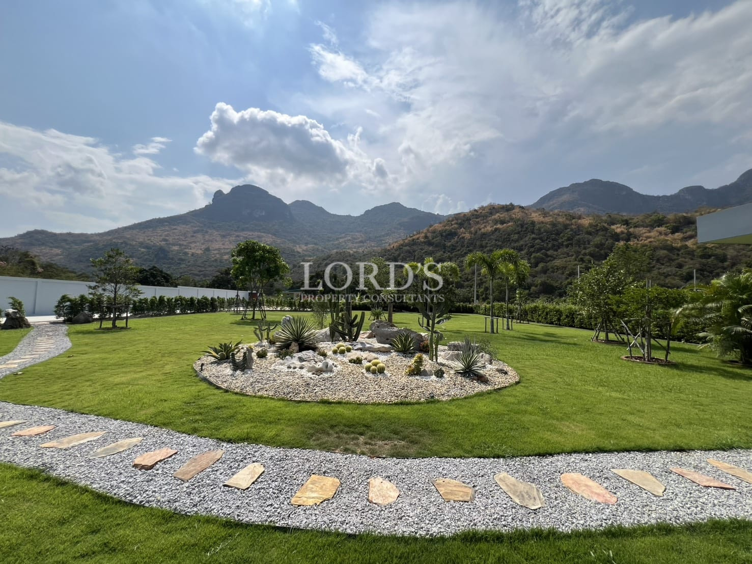 Landscaped garden with decorative cactus bed, stone pathway, and mountain backdrop.