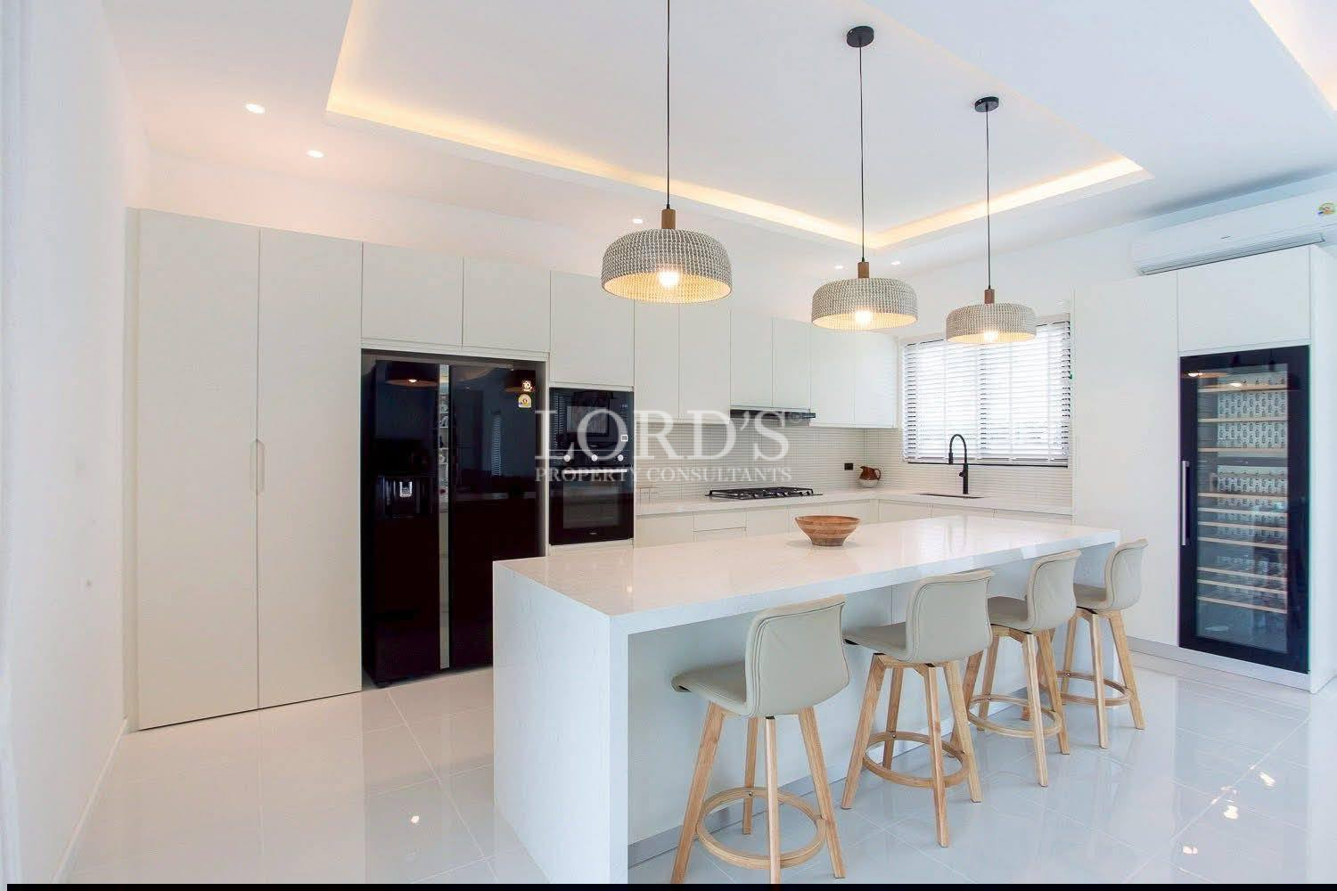Modern white kitchen with large island, bar stools, pendant lights, and built-in appliances.
