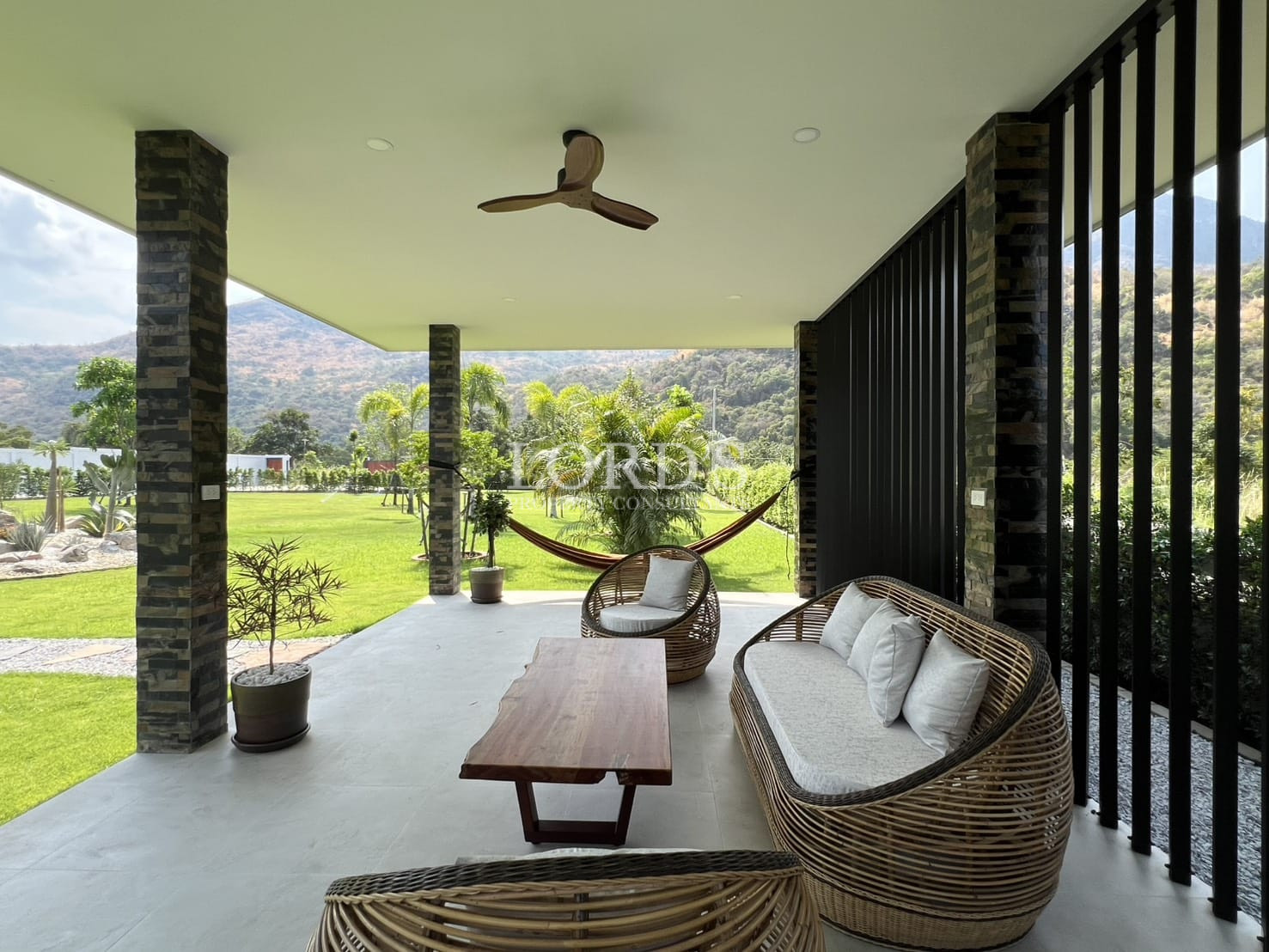 Covered outdoor terrace with wicker seating, hammock, and landscaped garden views.