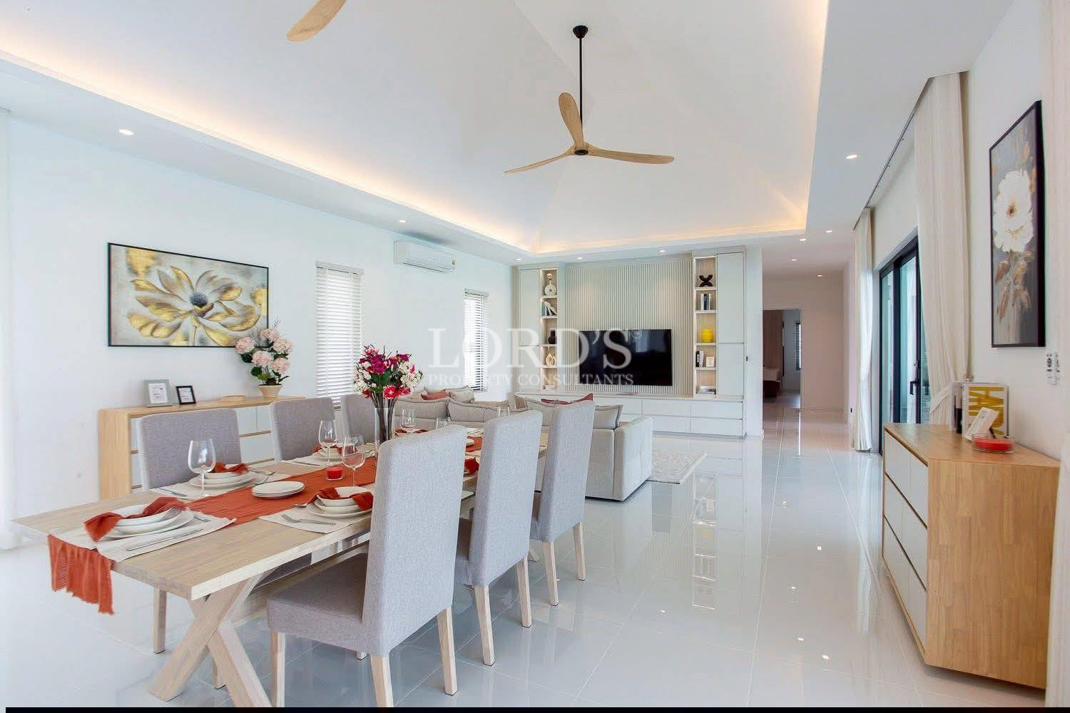 Modern open-plan dining and living area with set table, sectional sofa, and built-in TV wall.