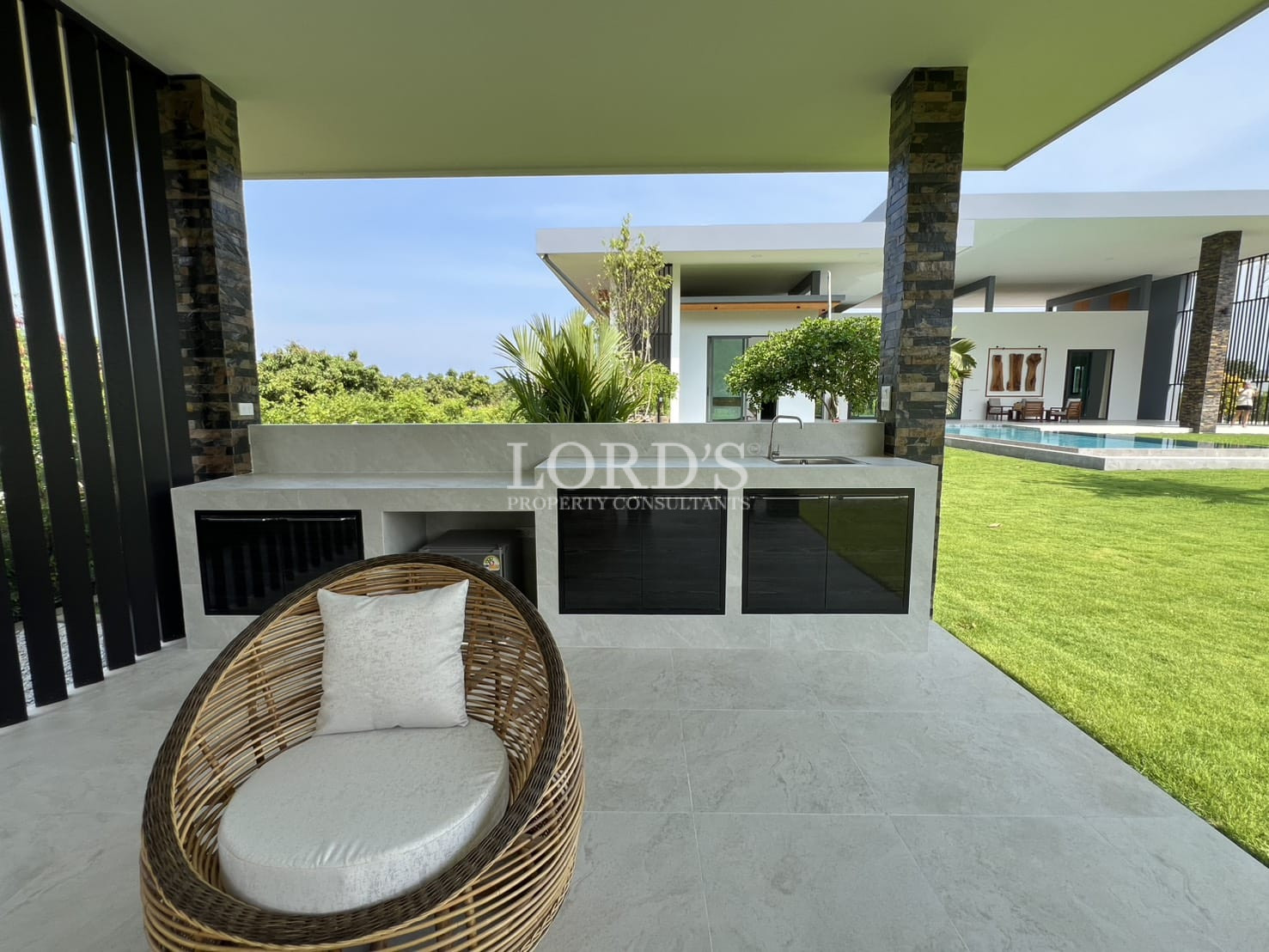 Outdoor covered patio with built-in kitchen counter, seating area, and garden view.