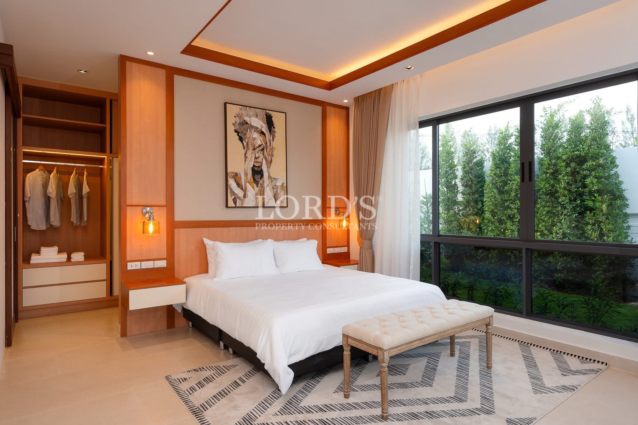 Modern bedroom with a queen bed, large window view, wooden accent wall, and open wardrobe.