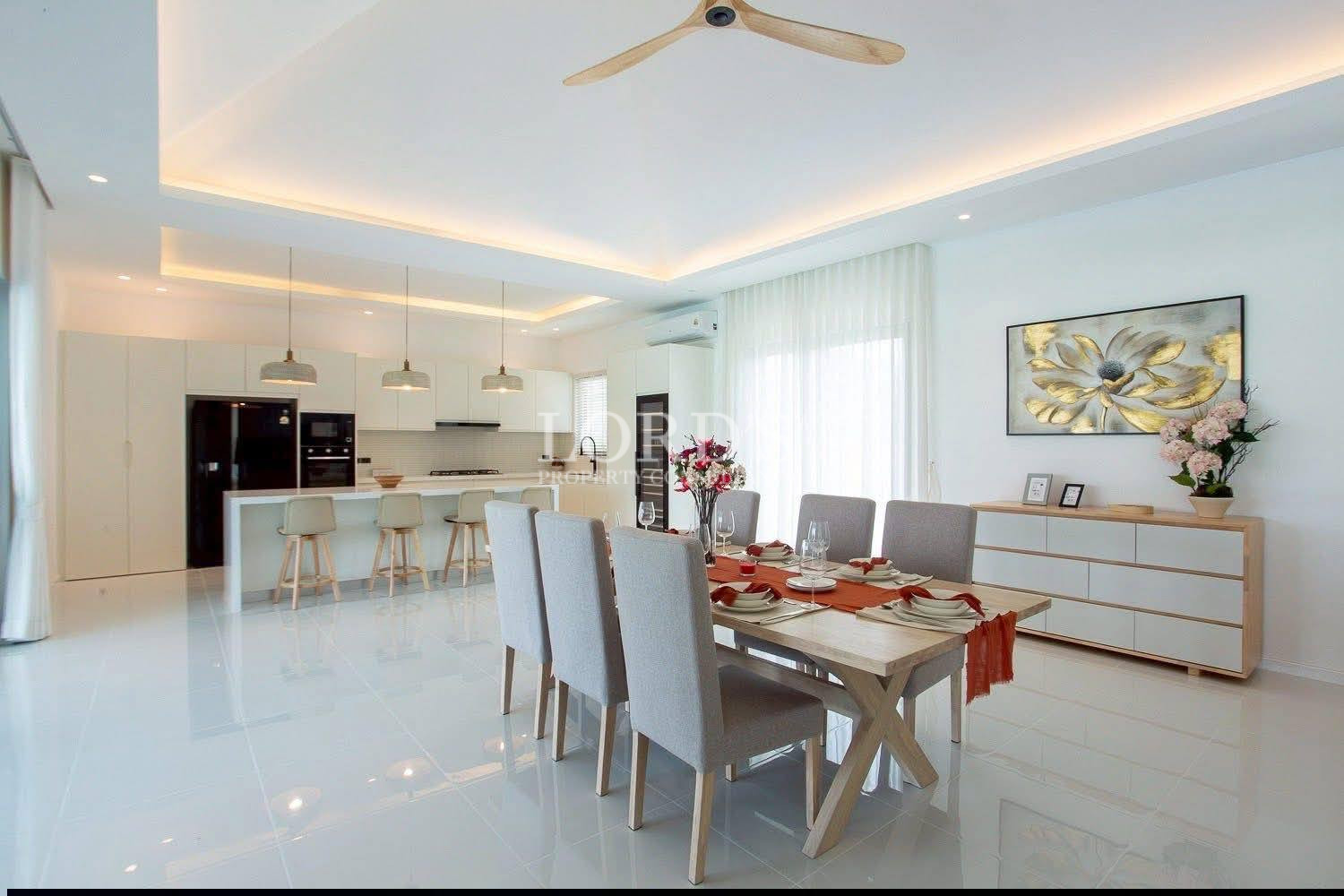 Modern open-plan dining area with set table, white kitchen island, and pendant lighting.