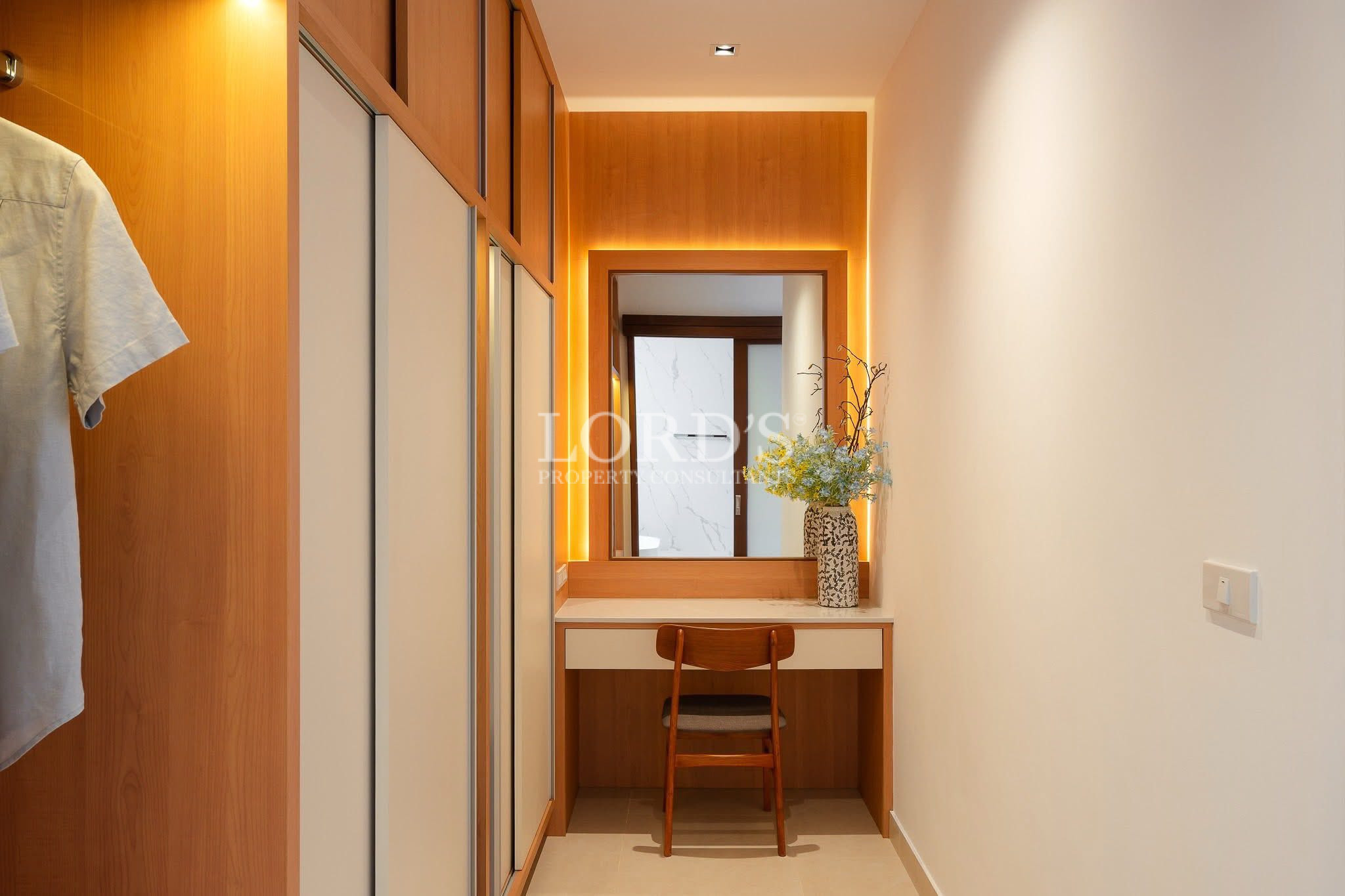 Walk-in wardrobe with built-in wooden closets and a vanity desk with mirror and warm lighting.