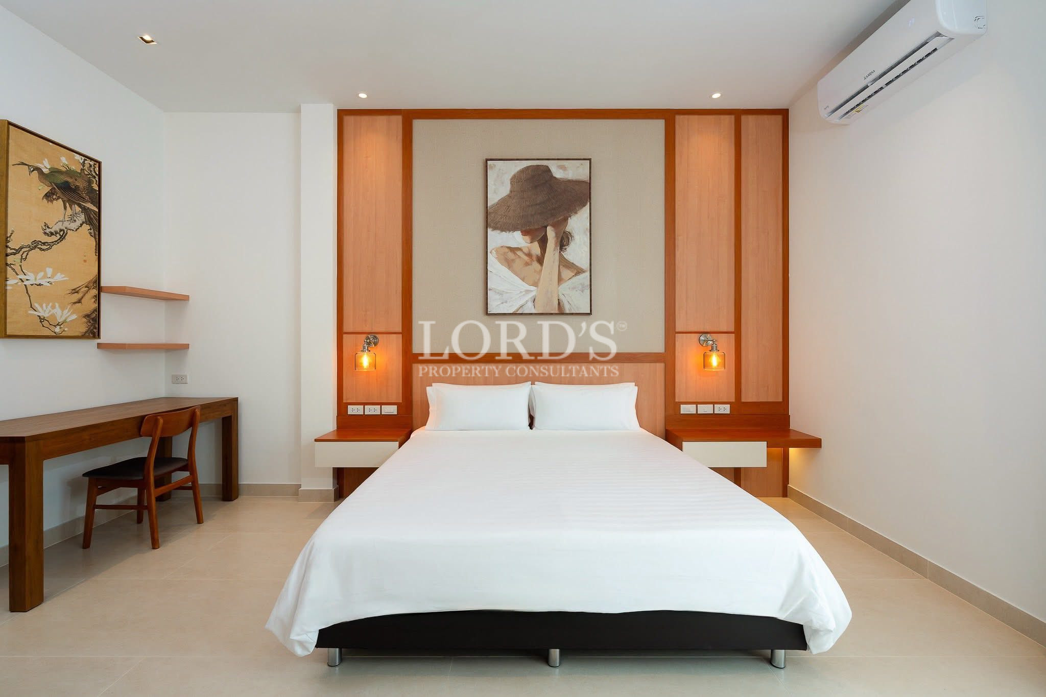 Modern bedroom with a queen-sized bed, wooden headboard with built-in lighting, bedside tables, and a workspace desk.