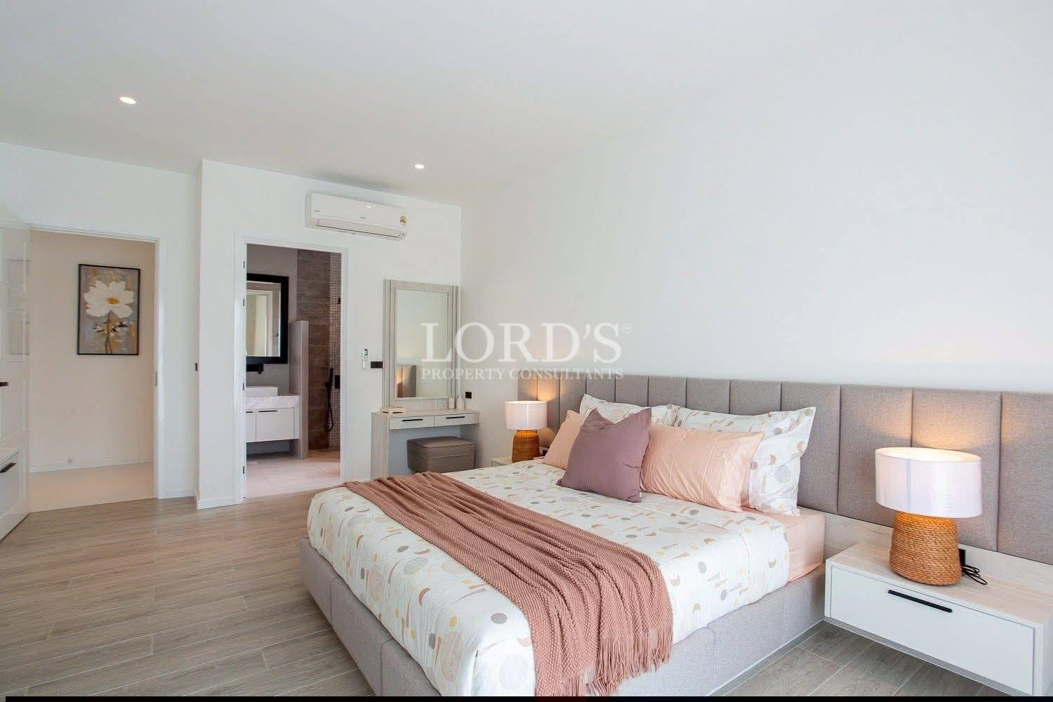 Modern minimalist bedroom with upholstered bed, bedside lamps, wooden flooring, and en-suite bathroom