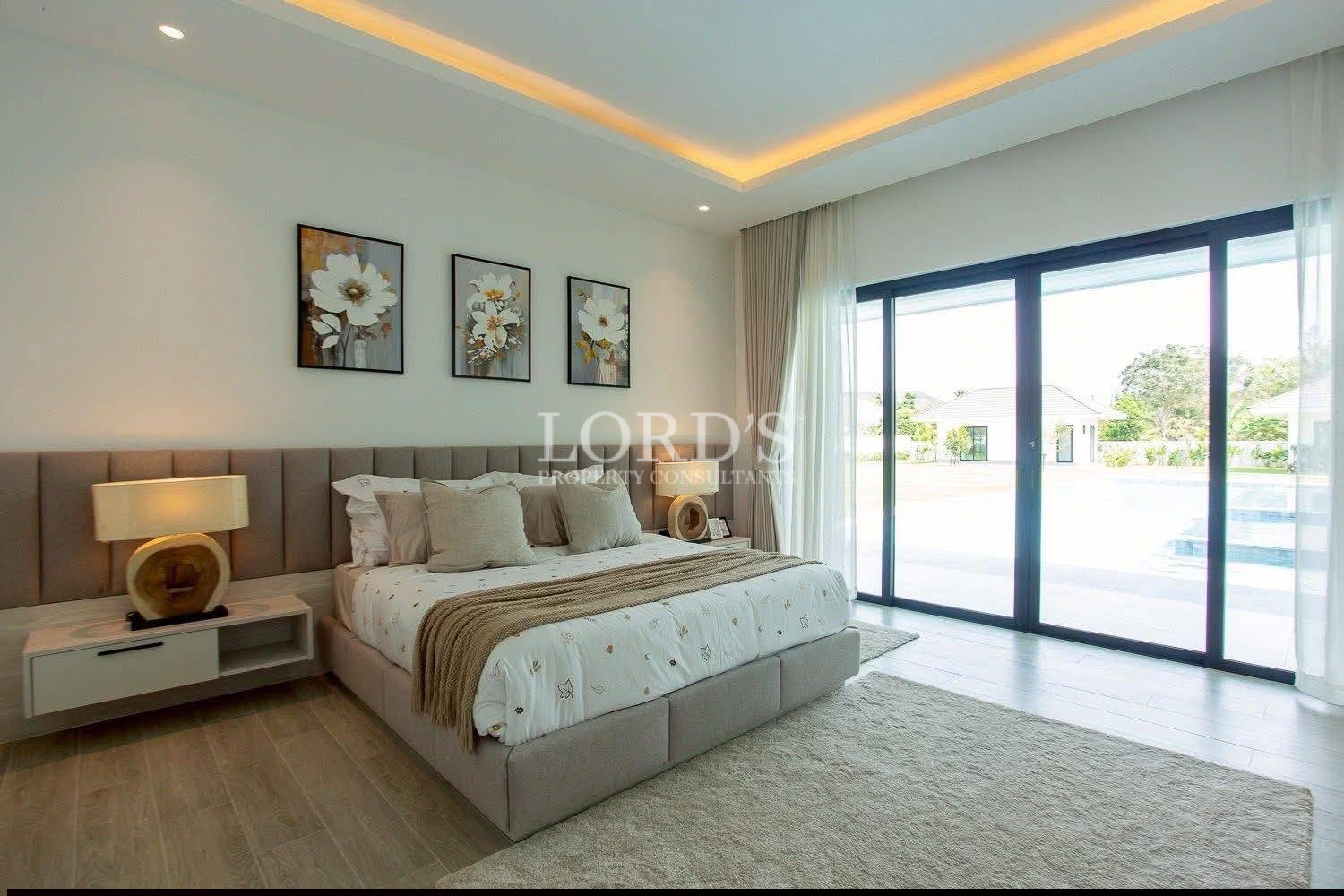 Modern bedroom with upholstered bed, floral wall art, and large sliding glass doors overlooking pool.
