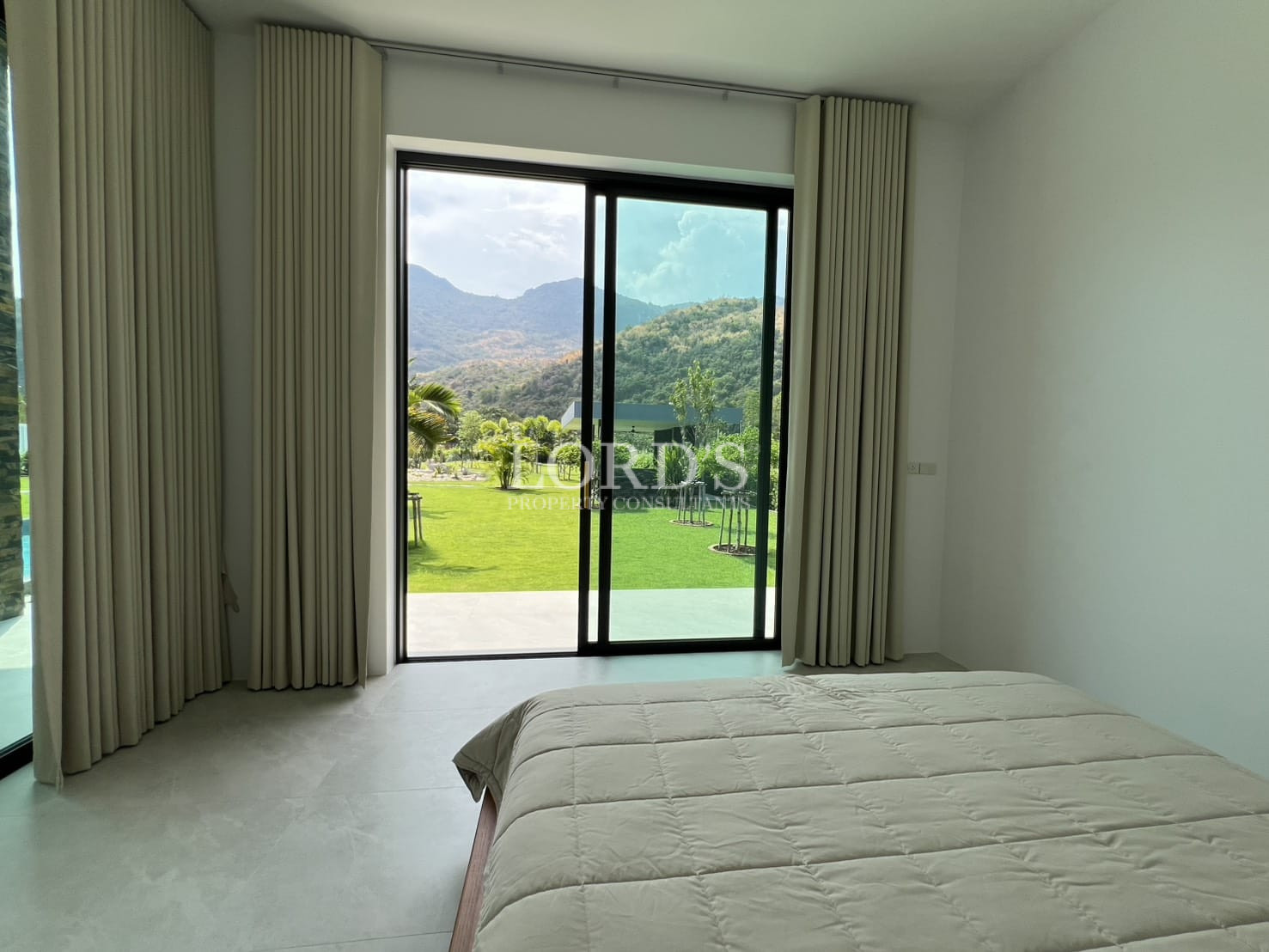 Modern bedroom with sliding glass doors opening to a landscaped garden and mountain view.
