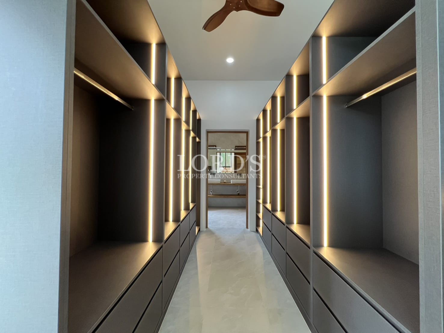 Contemporary walk-in closet hallway with dark built-in wardrobes, drawers, and integrated vertical LED lighting.