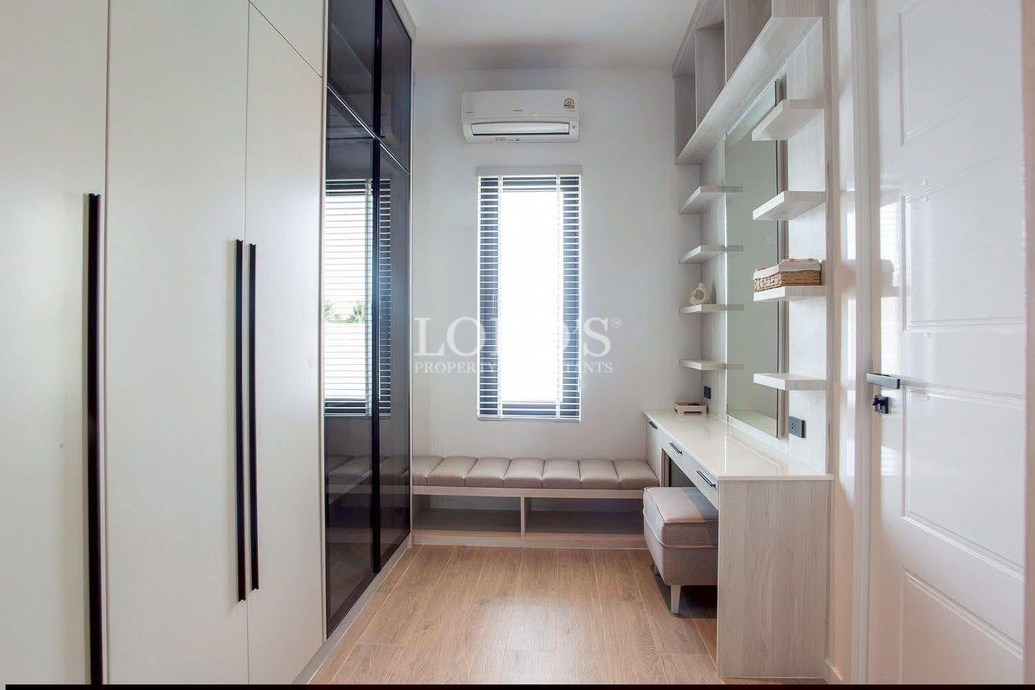Modern walk-in closet with built-in wardrobe, vanity desk, shelving, and window seating bench.