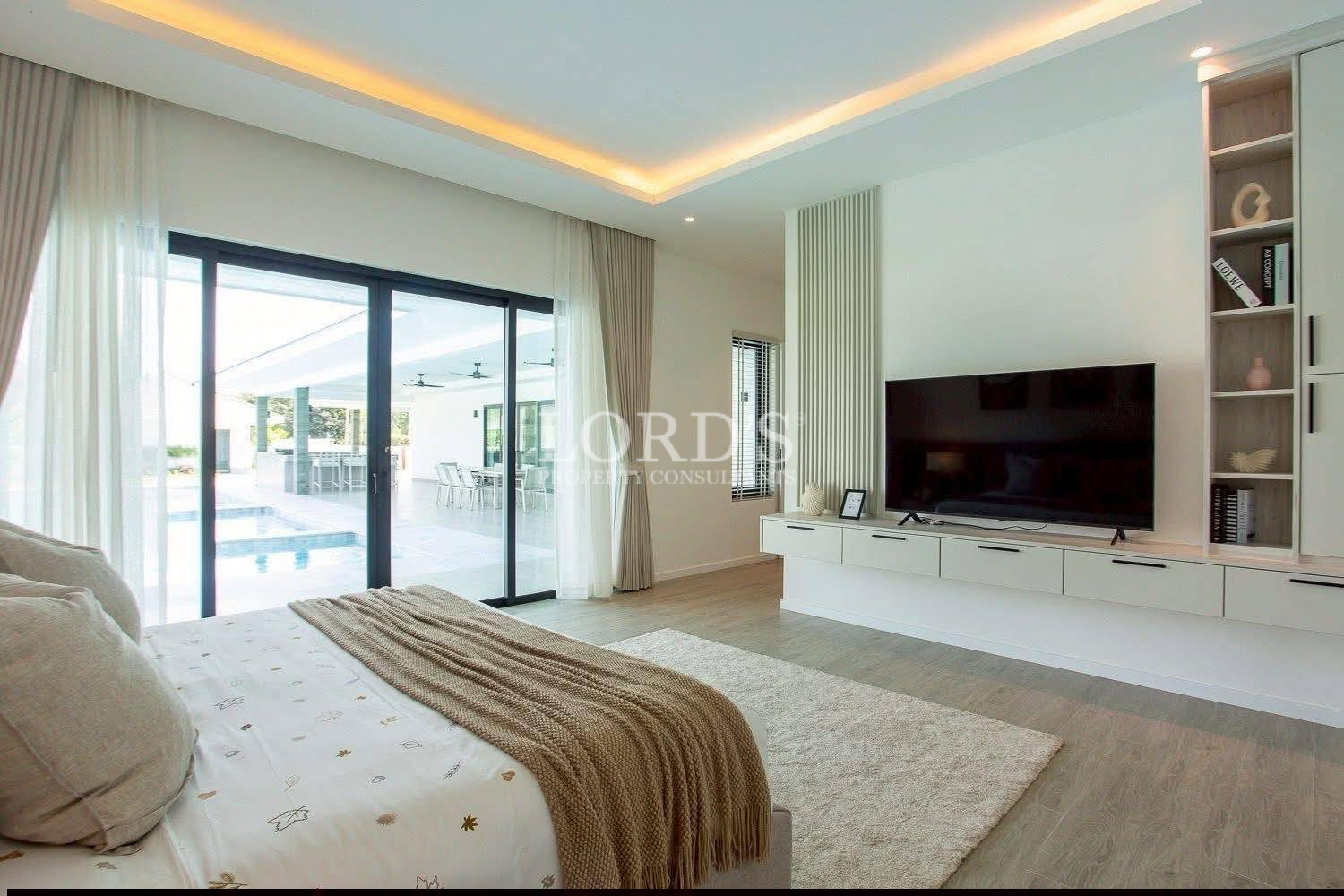 Modern bedroom with sliding glass doors, built-in TV unit, and view of outdoor pool area.