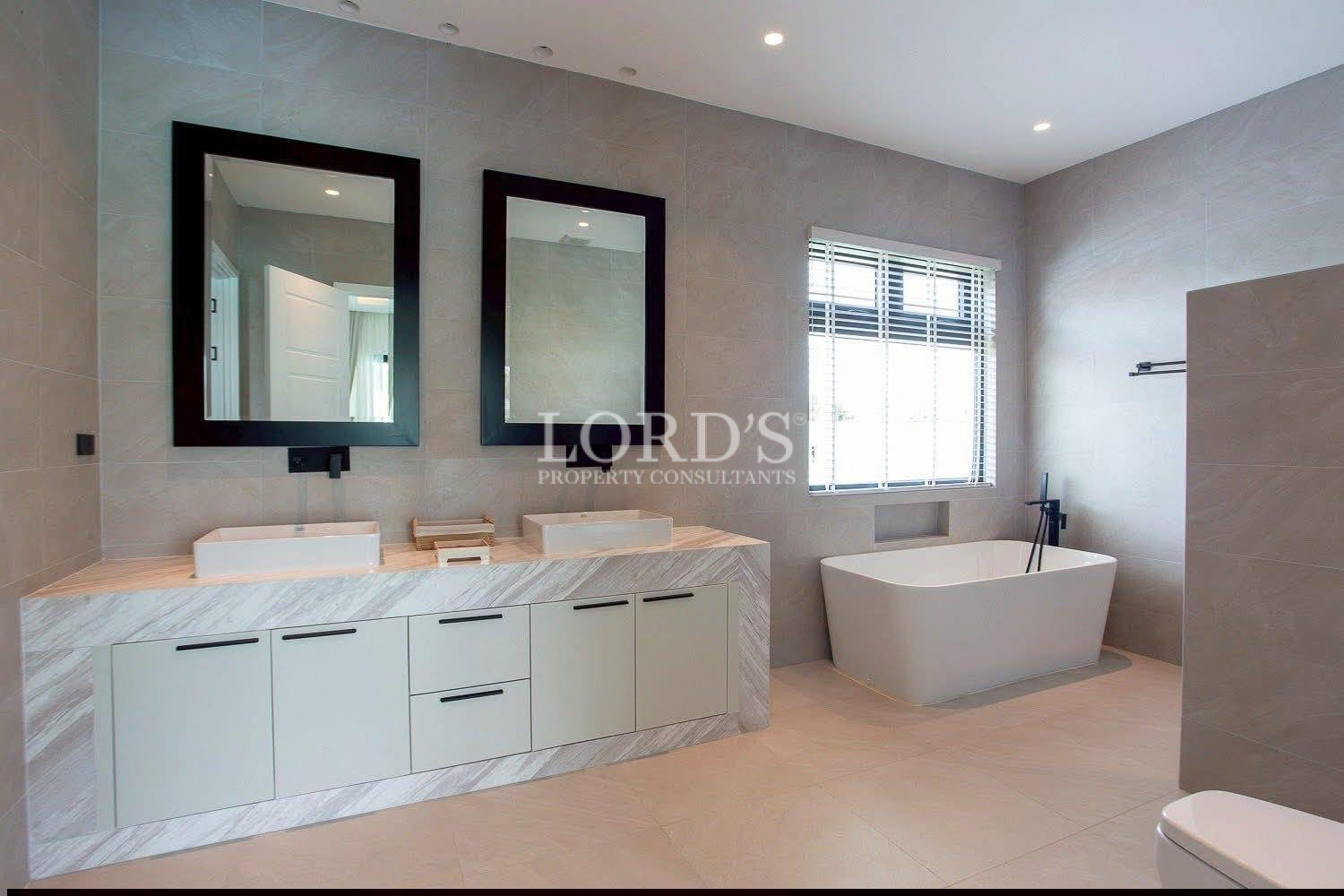 Modern luxury bathroom with double vanity sinks, black framed mirrors, marble countertop, and freestanding bathtub.