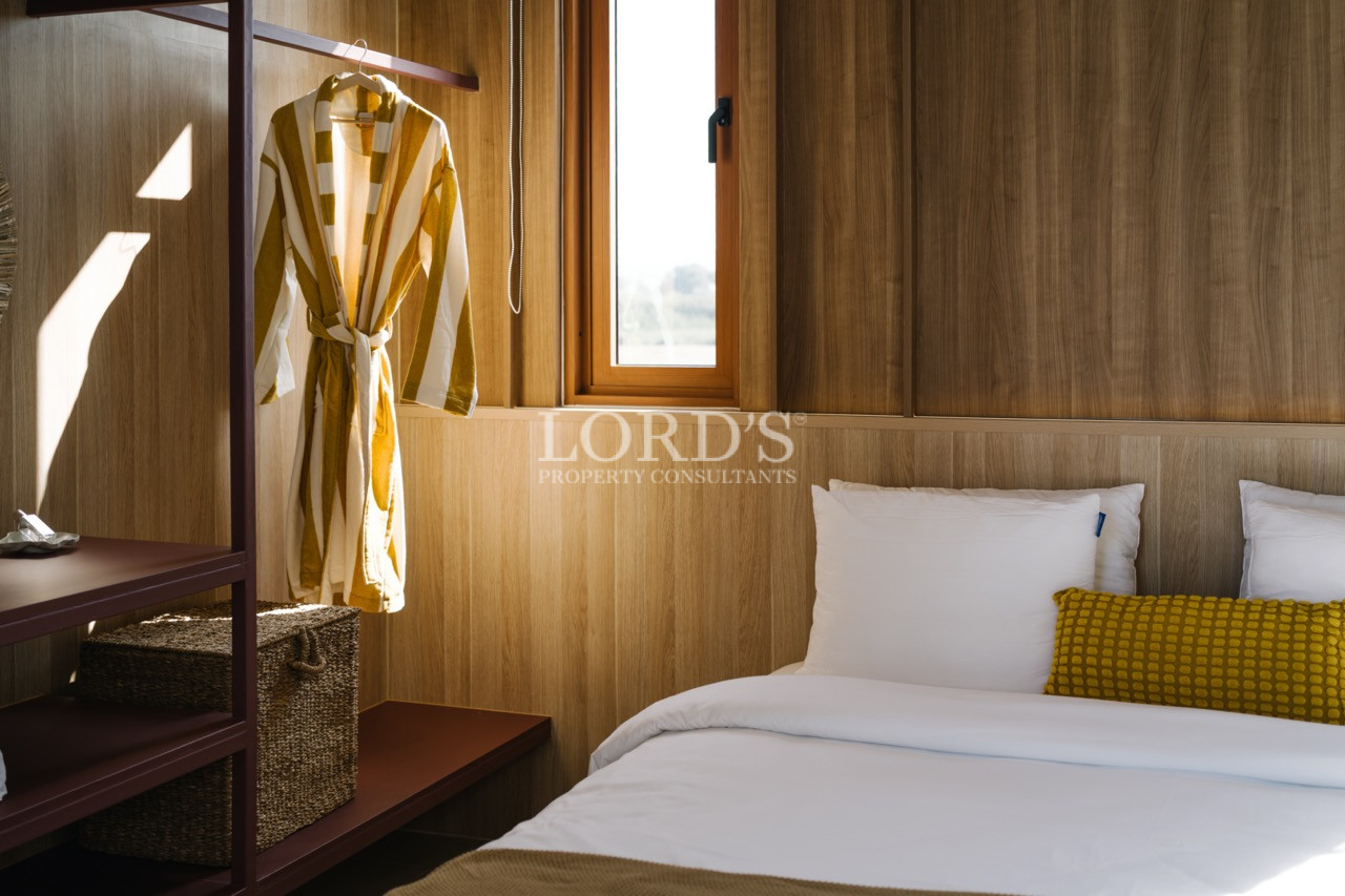 Cozy bedroom with wood-paneled walls, white bedding, and a striped robe hanging beside a window.