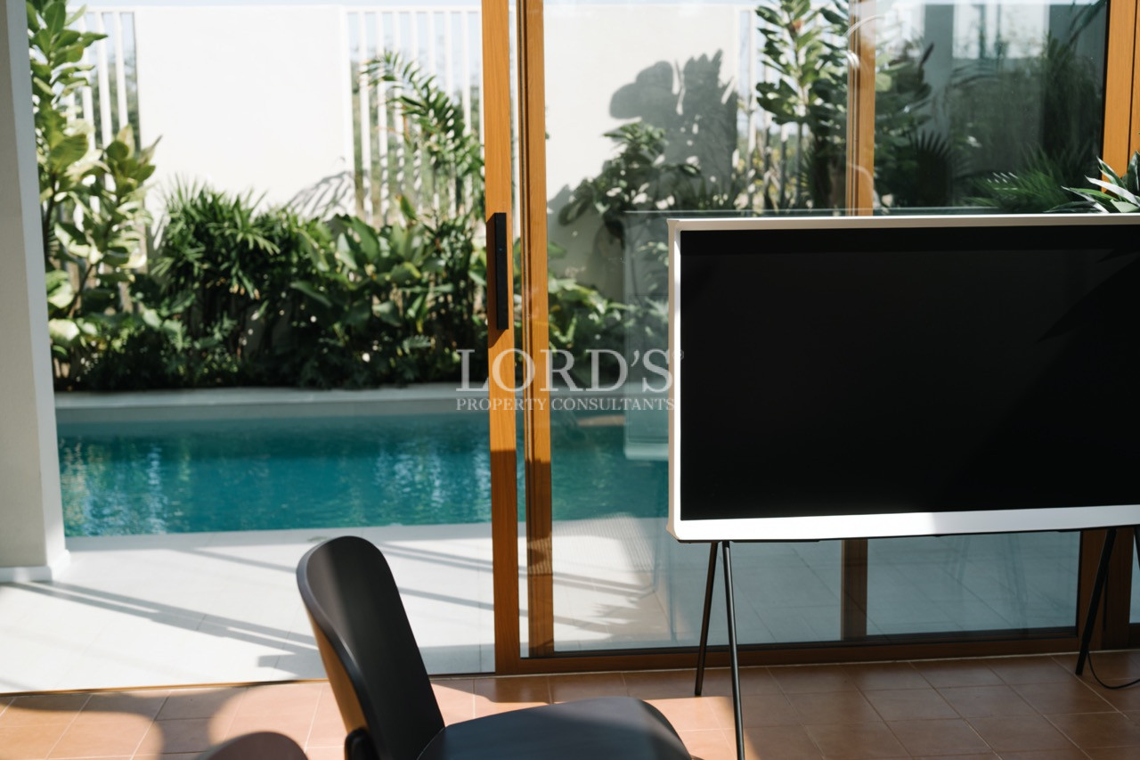 Modern television on a stand in front of glass doors overlooking a private pool and lush greenery.