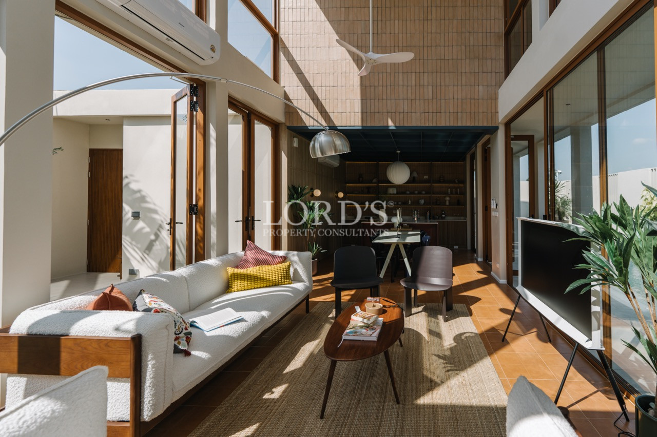 Sunlit modern living room with white sofas, wood accents, and open glass doors leading to a courtyard.