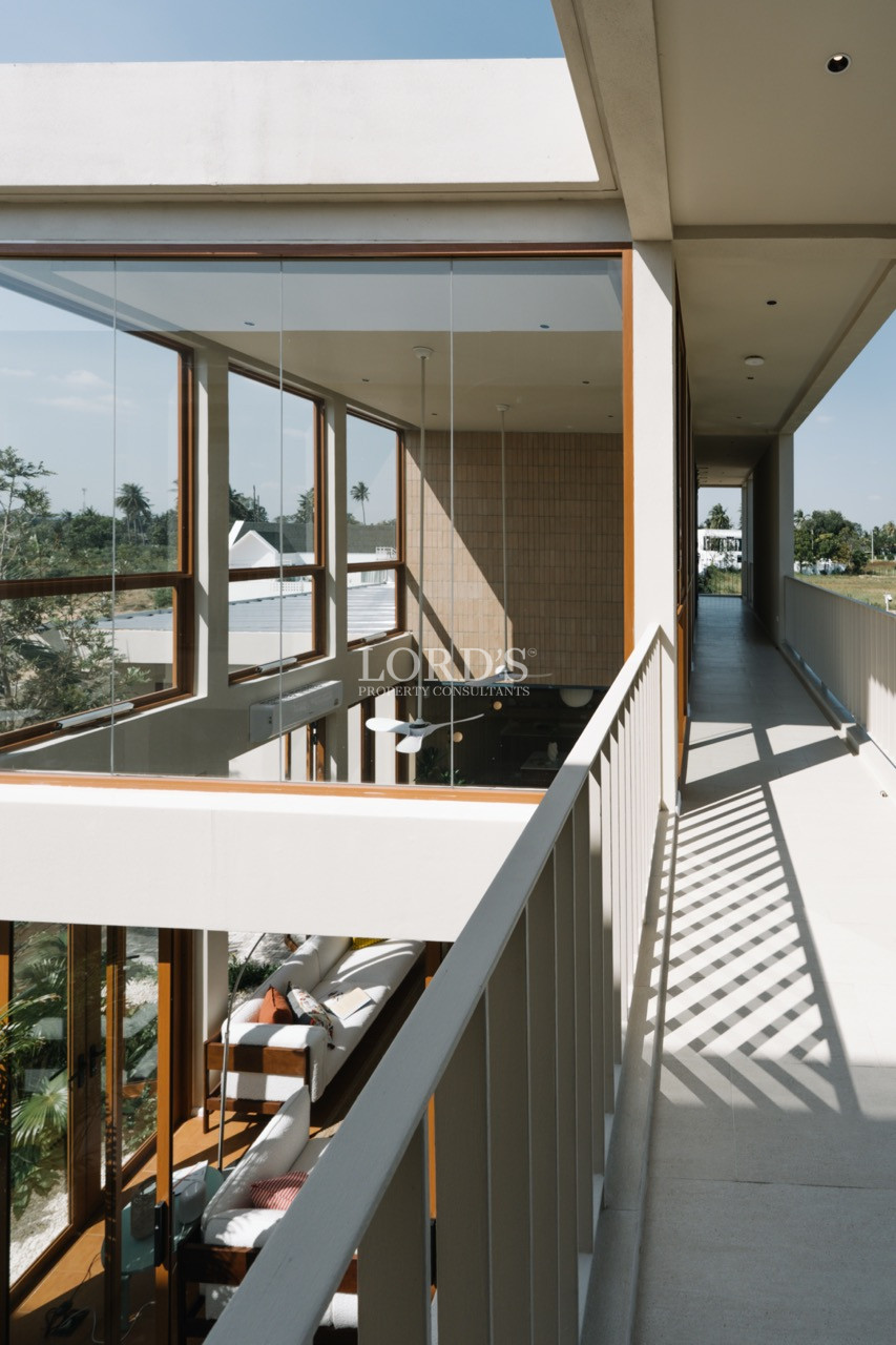 Upper-level balcony corridor with glass railing overlooking a double-height living space.