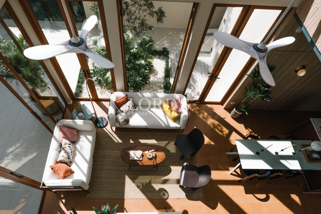Top-down view of a bright living and dining area with sofas, coffee table, and large glass doors.