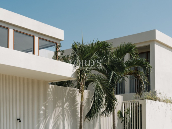 Contemporary white two-story house with palm trees against a clear blue sky.