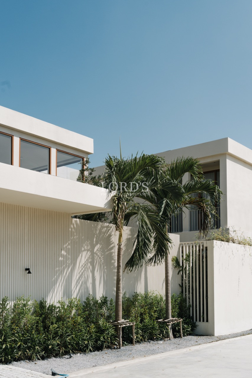 Contemporary white two-story house with palm trees against a clear blue sky.