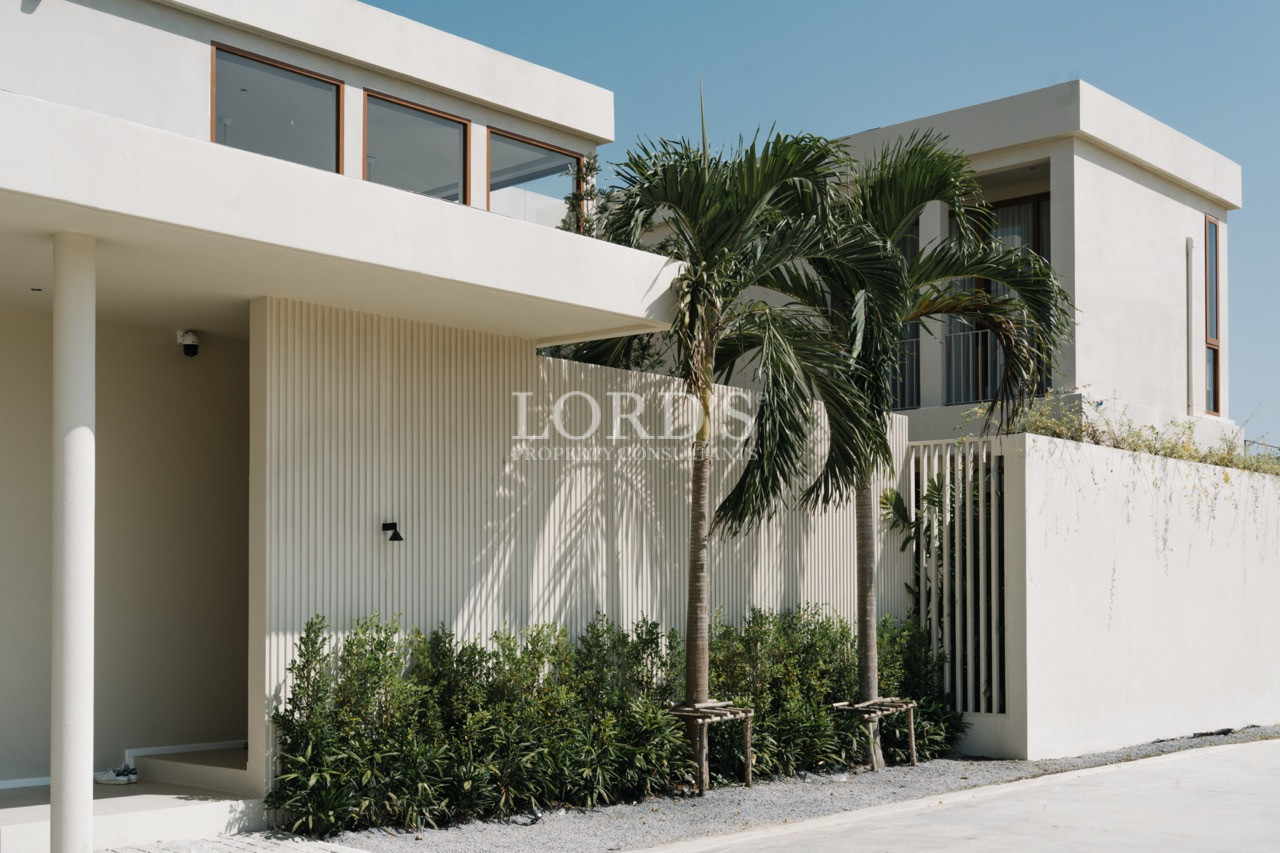Modern two-story white house exterior with palm trees and minimalist landscaping.