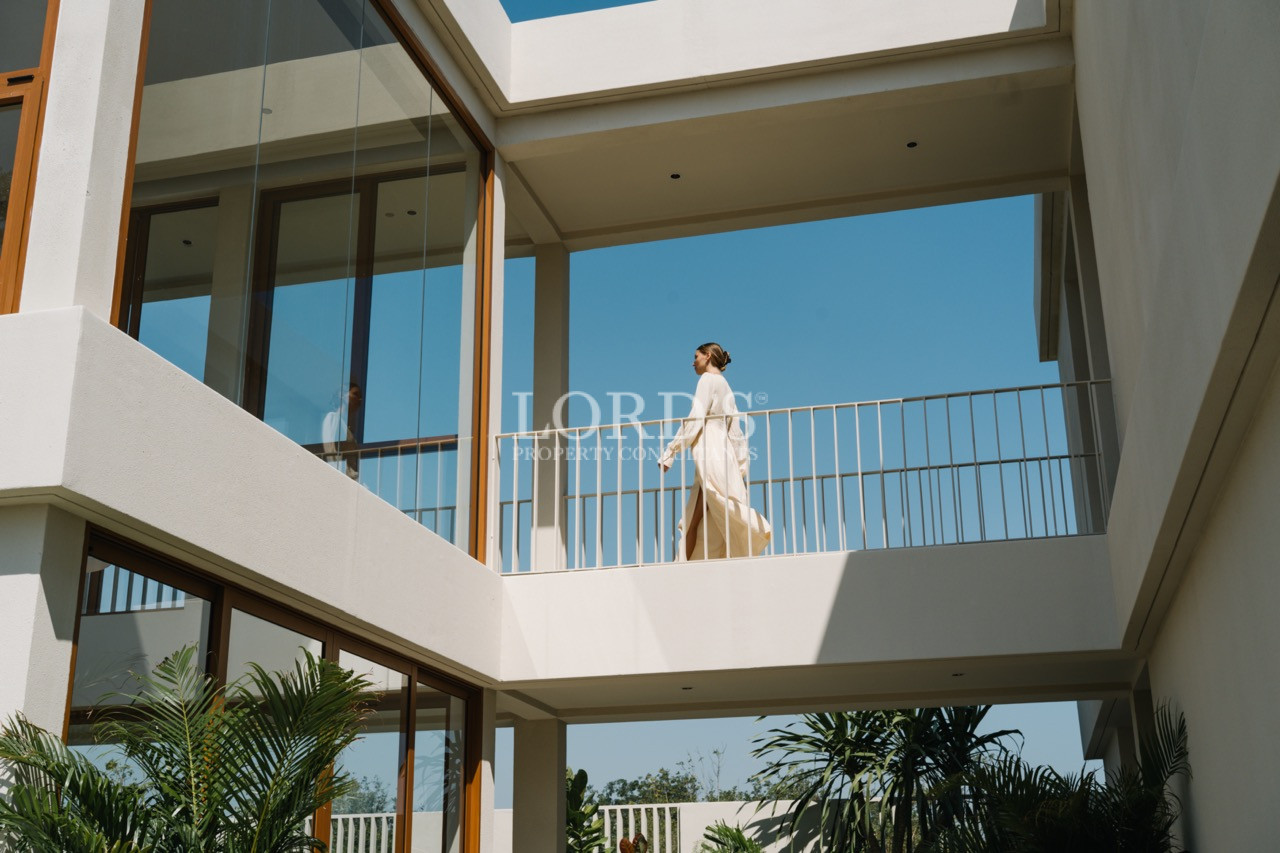 Modern two-story home with glass windows and a woman walking along the upper balcony.