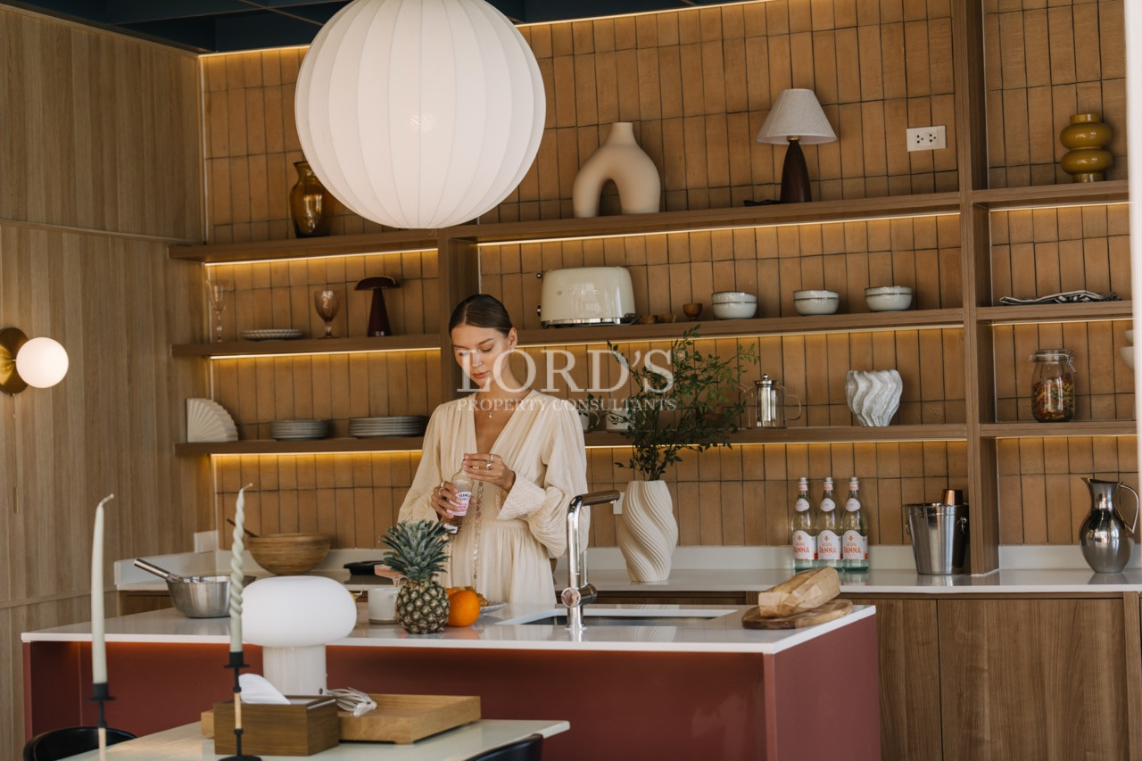 Modern kitchen with wooden shelving and a woman preparing a drink at the island counter.