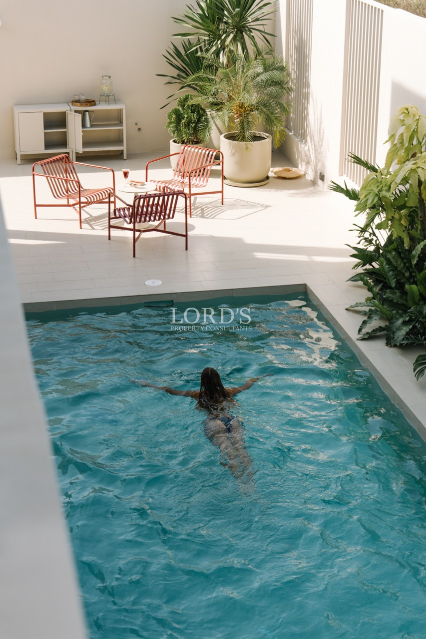 Private courtyard pool with a person swimming and red outdoor chairs on a sunlit terrace.