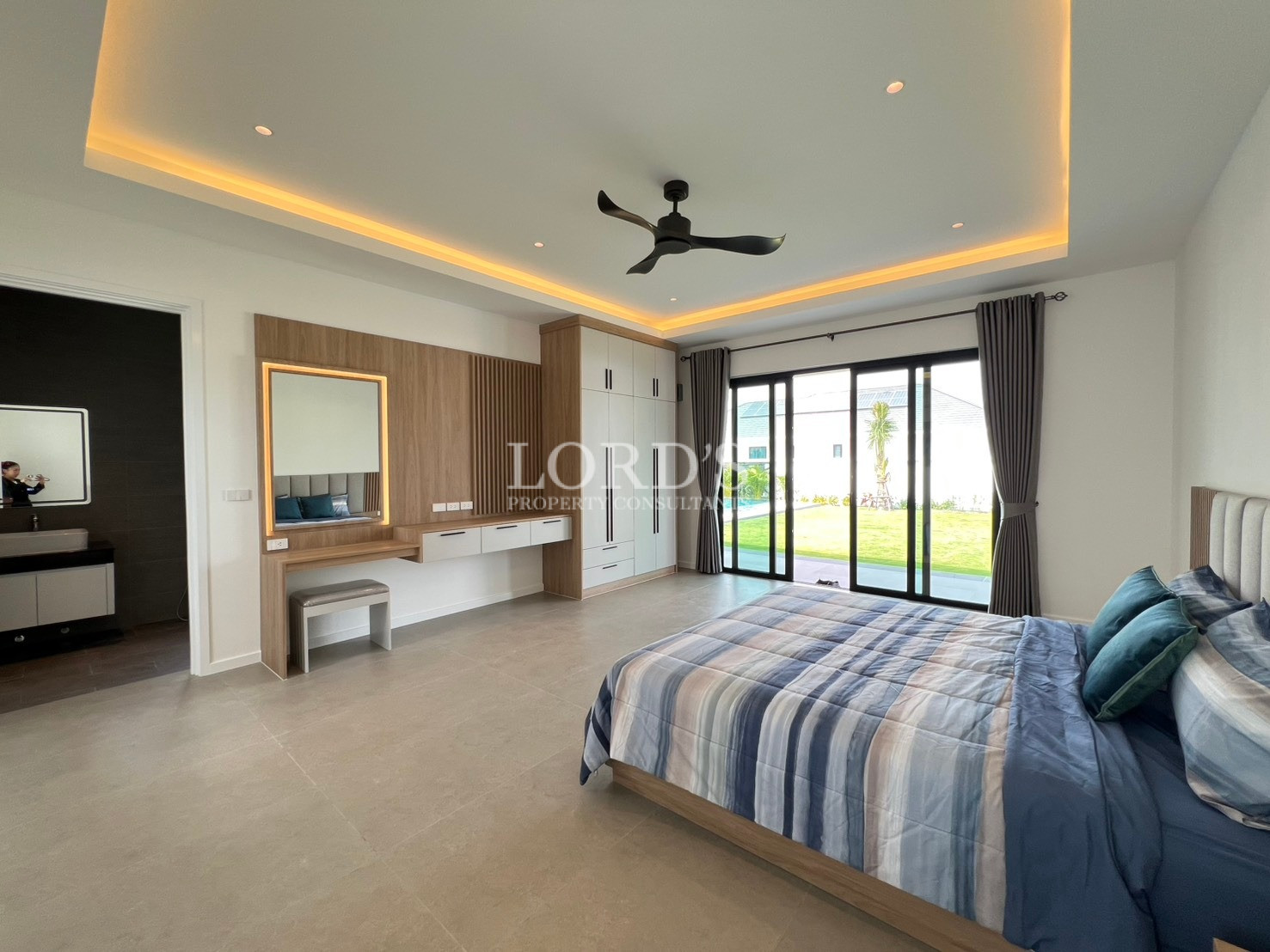 Spacious modern bedroom with large bed, vanity table, built-in wardrobe, and sliding glass doors to garden.