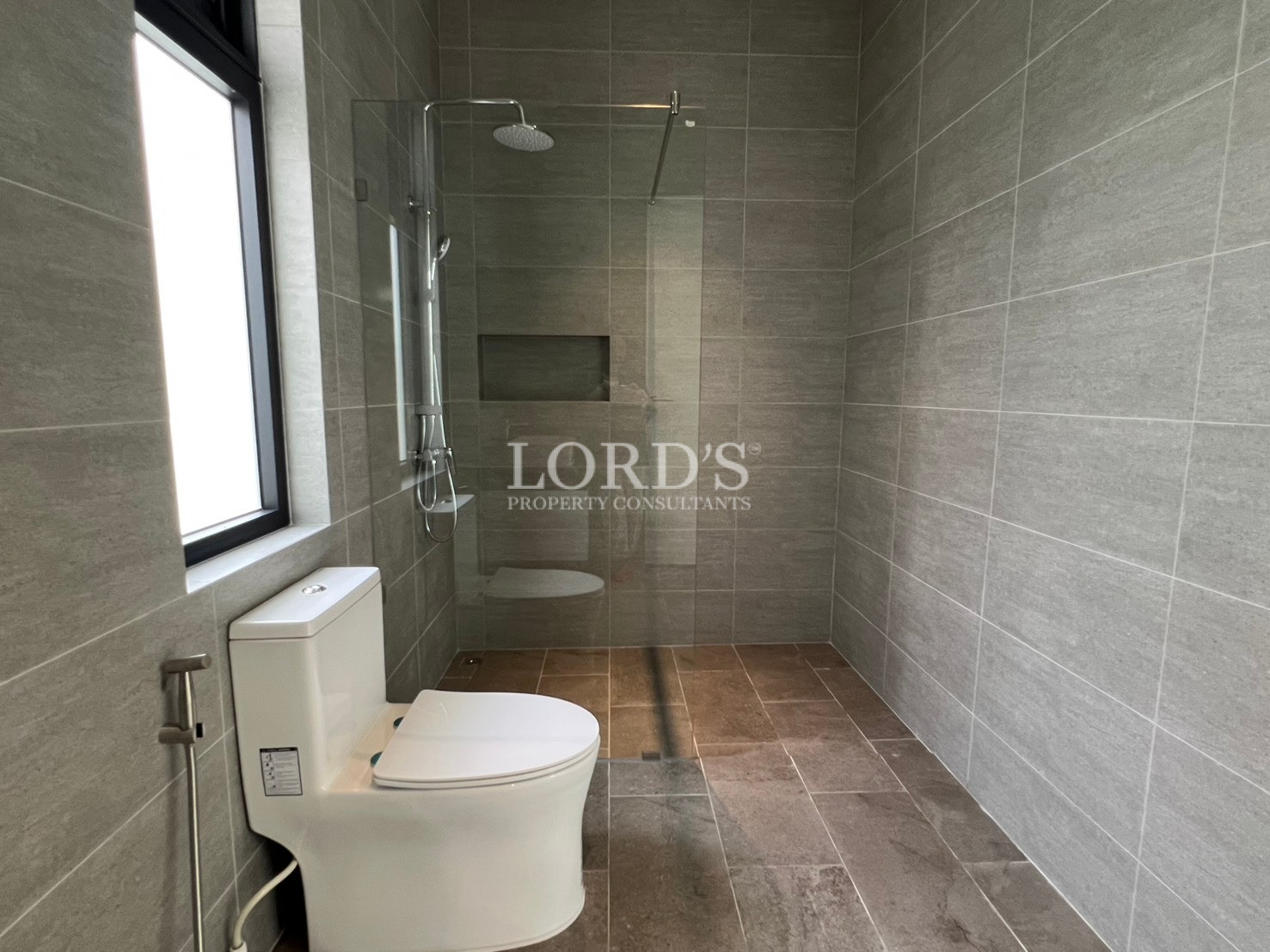 Modern bathroom with toilet, walk-in glass shower, and grey tiled walls.