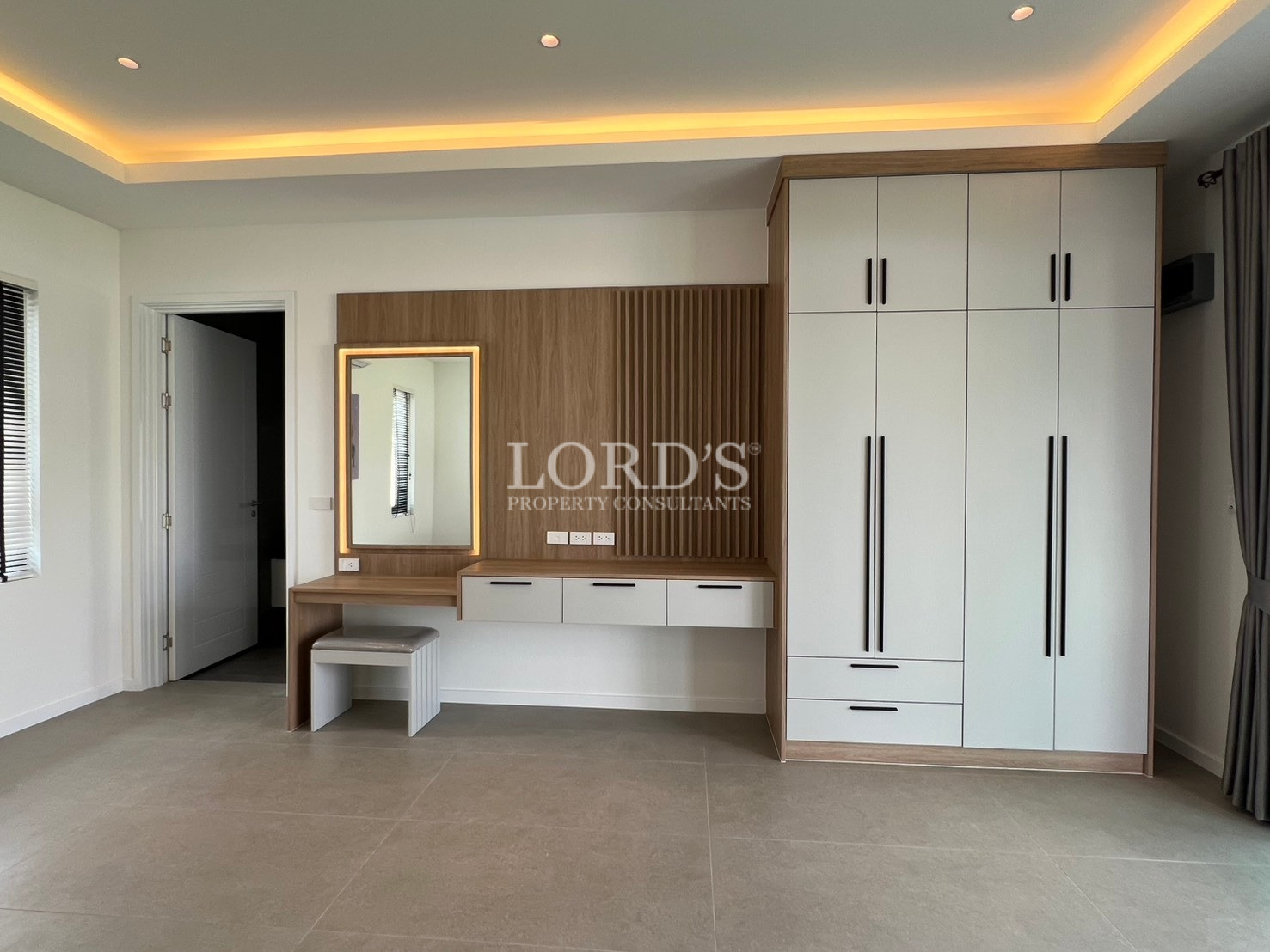 Modern bedroom dressing area with built-in wardrobe, vanity table, and illuminated mirror.