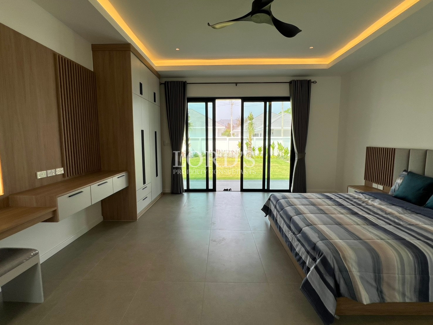 Spacious modern bedroom with large sliding glass doors, built-in wardrobe, and garden view.