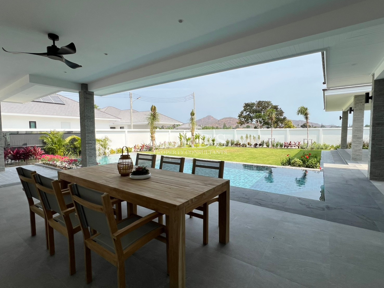 Covered terrace with outdoor dining table overlooking private pool and garden
