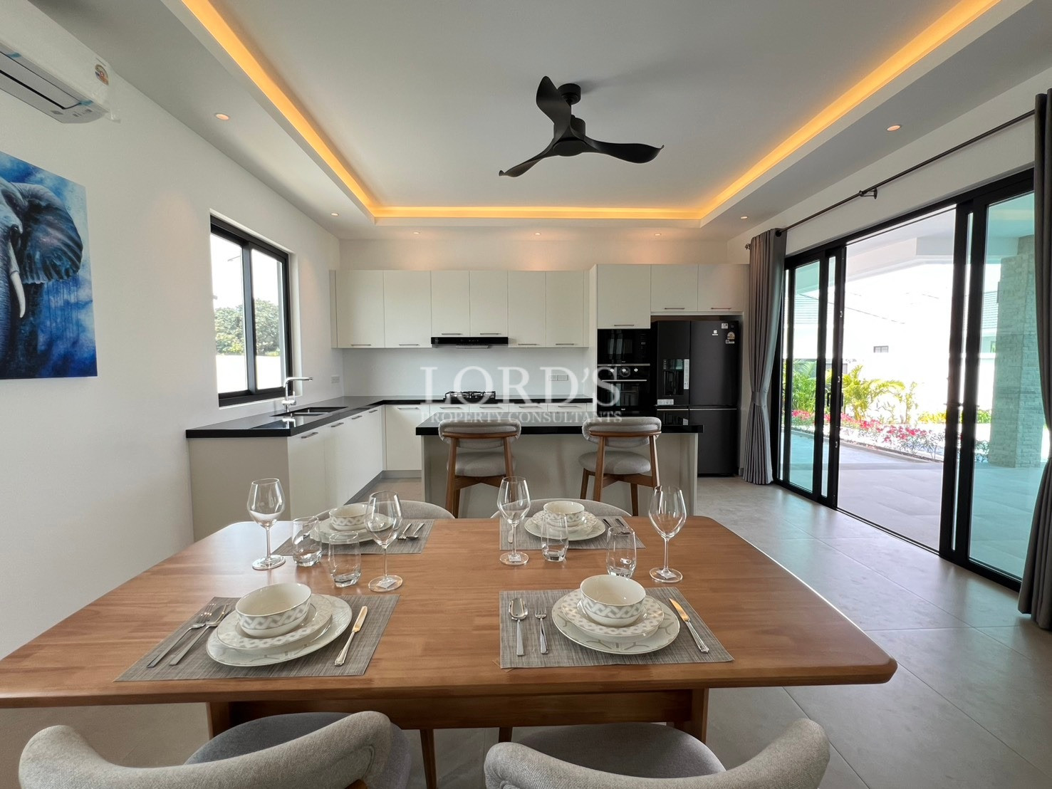 Modern open-plan kitchen and dining area with wooden dining table, island counter, and large glass sliding doors.