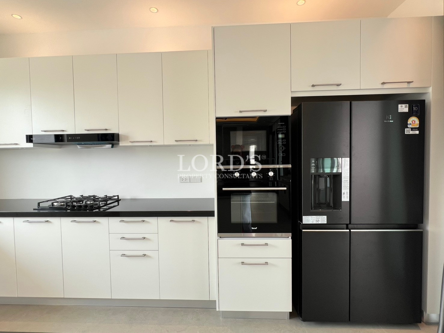 Modern kitchen cabinets with built-in oven, gas stove, and large black double-door refrigerator.